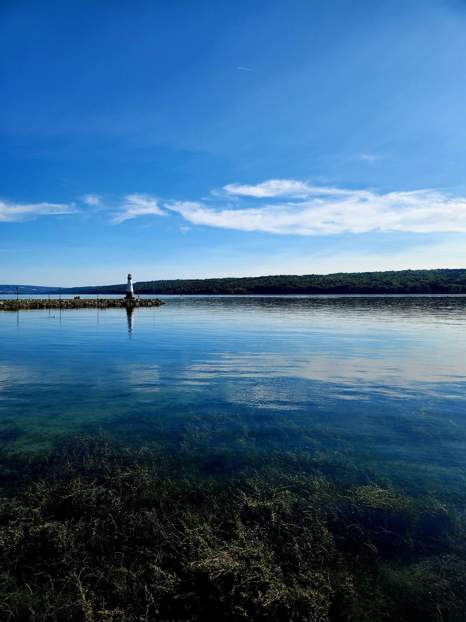 Blue water in the bottom half, a light house in the distance (mid picture) and blue skies with white clouds at the top.