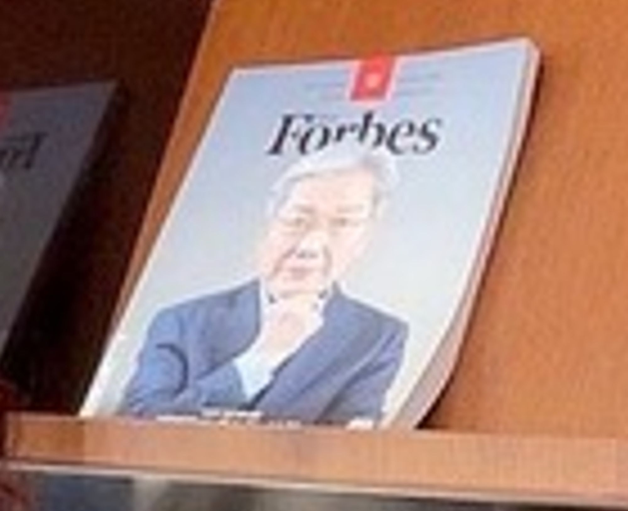 A photo of a Forbes magazine on a library shelf, with an older man with white hair on the cover.