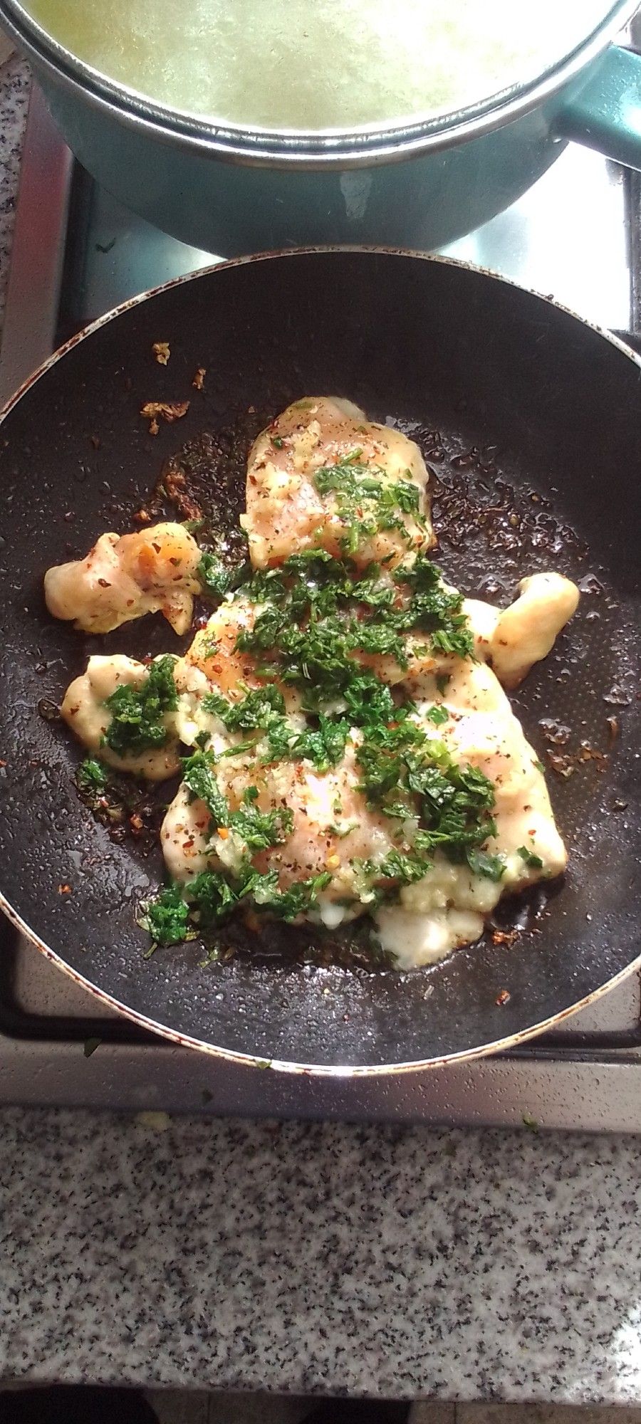 pollo al perejil in a frying pan, and some rice cooking in a pot nearby