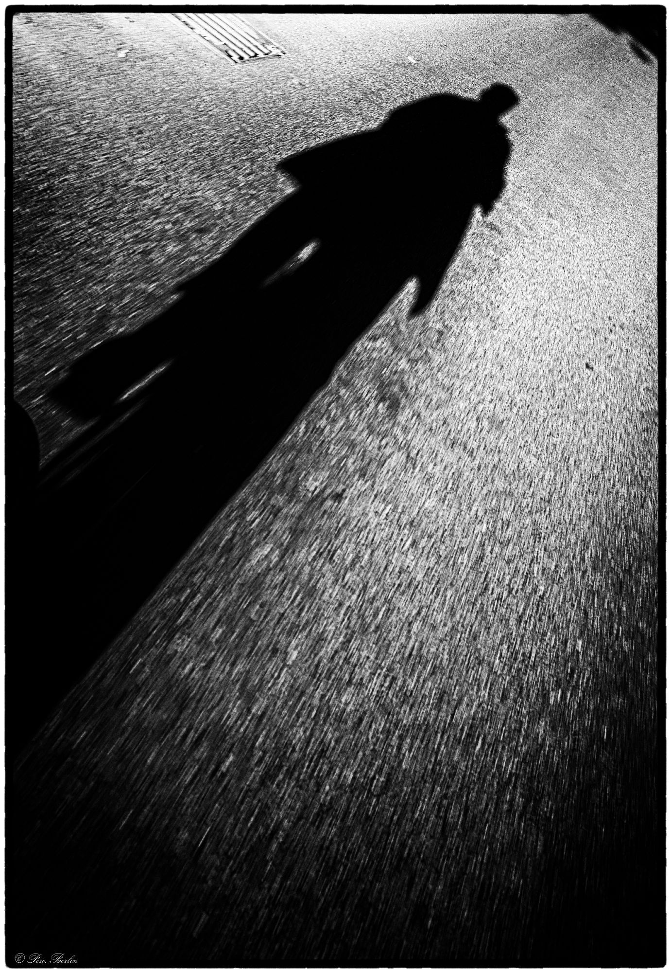 Black and white photograph of the long shadow of a cyclist on the asphalt.