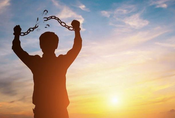 person breaking chains in front of a sunset