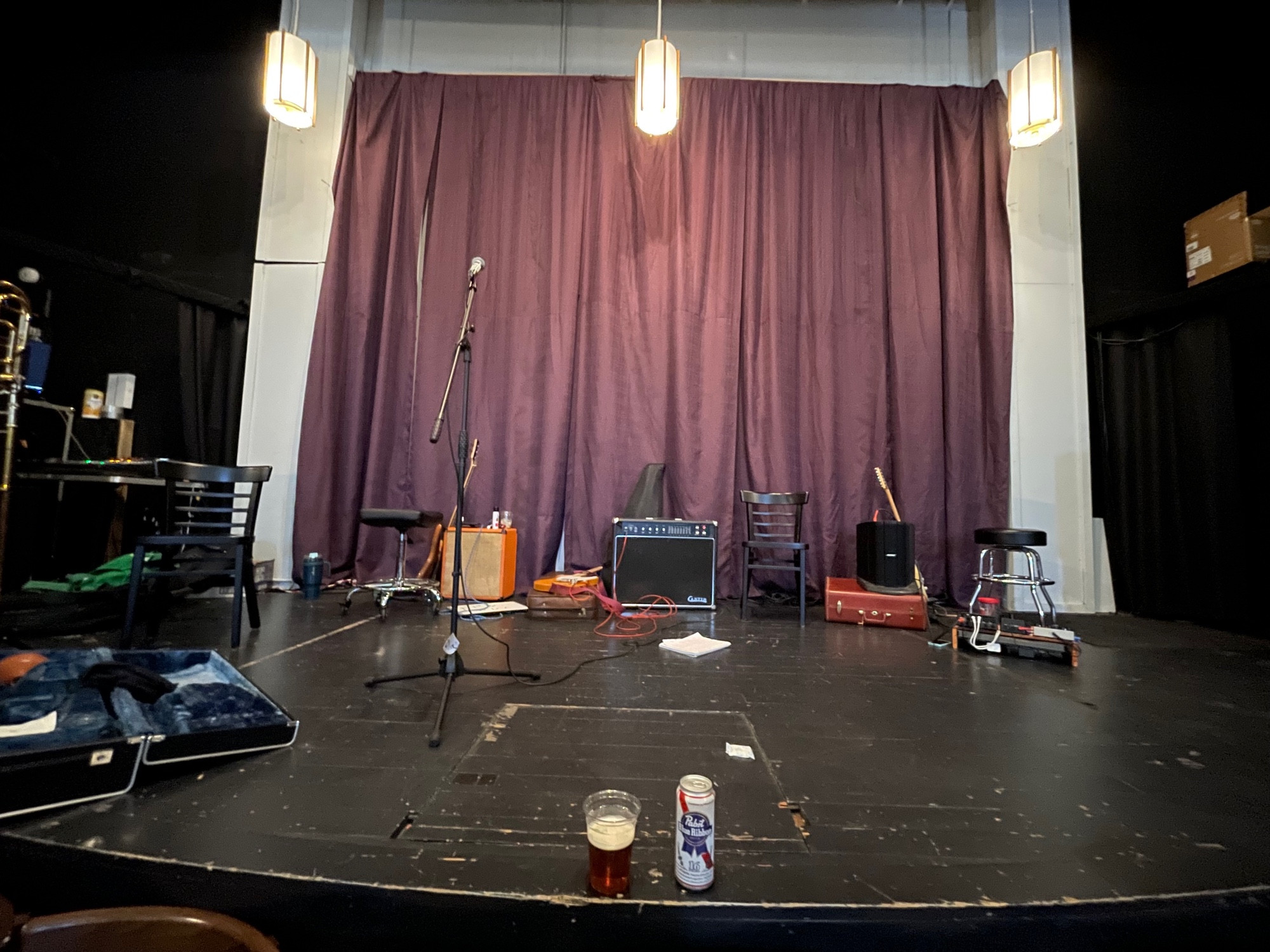 The stage, black floor with a couple beers, amps, and guitars in front of a wine-dark curtain 