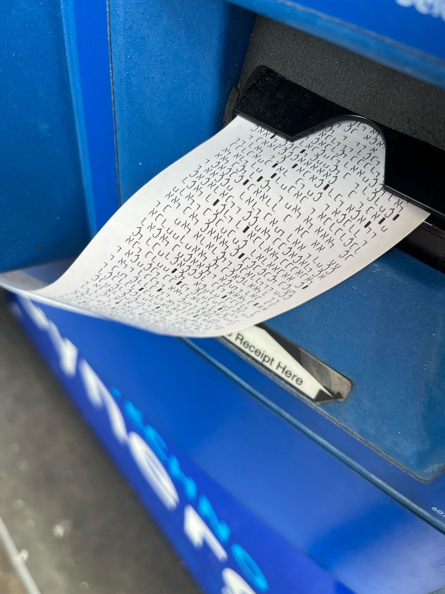 A close up of a receipt coming out of a gas pump. It has nonsense characters, mostly non-English-alphabet, printed on it.