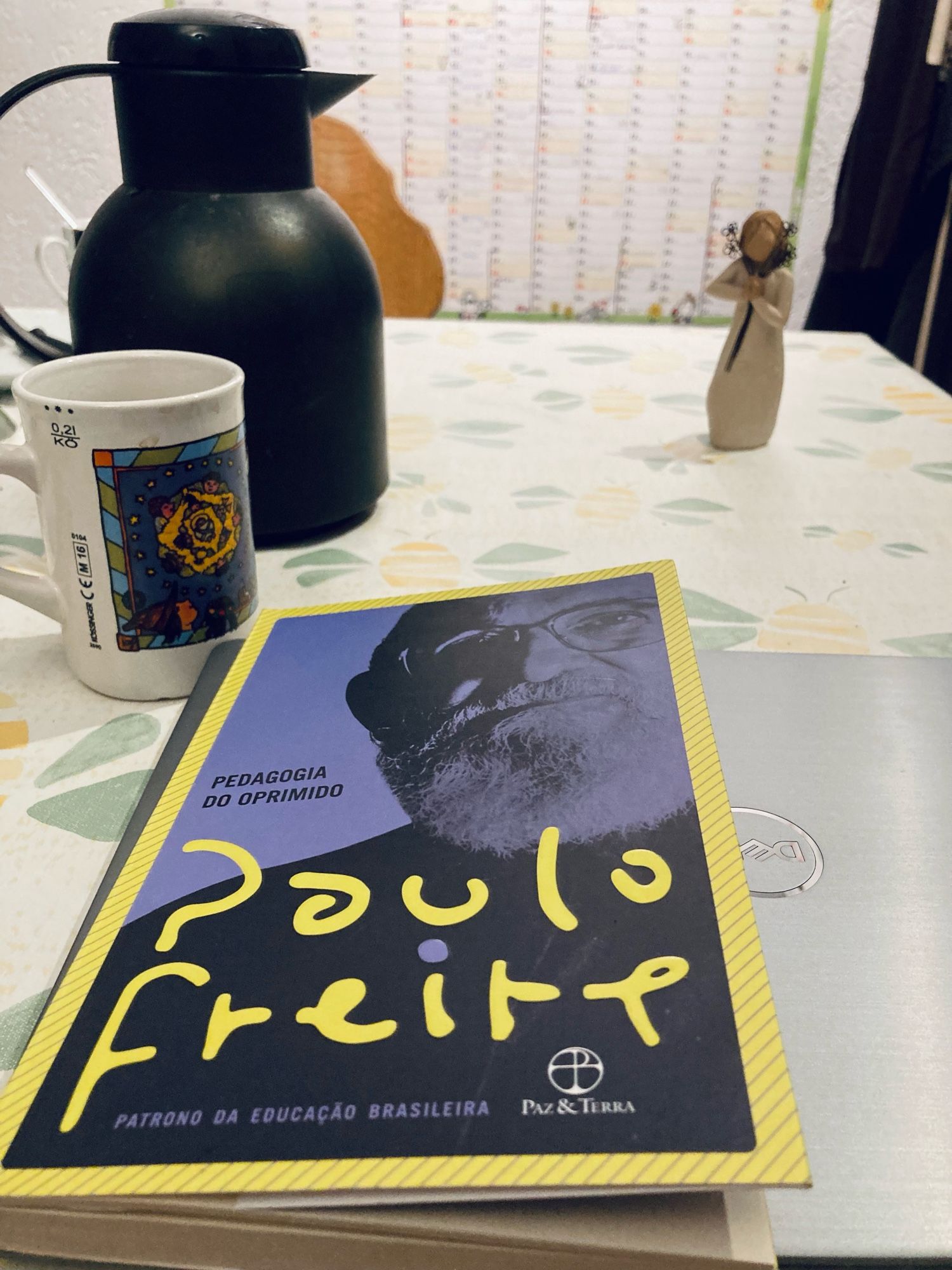 Livro de Paulo Freire “Pedagogia do oprimido” sobre um laptop. Uma garrafa e uma xícara de café a esquerda.