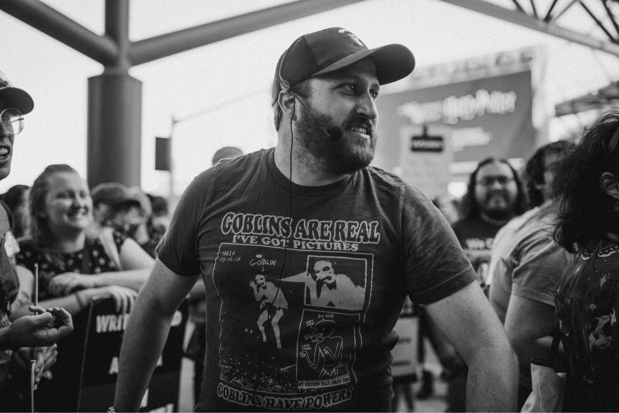 Black and White photo of me, beard could use a bit of a trim,  but let’s call it a “strike beard” and move on. I’m facing the right, with a more angry than usual sneer, as I square up against some unknown foe. my shirt says “Goblins are real, I’ve got pictures” with a picture that is like a crouching person with a triangle nose, who is definitely not a goblin. There’s a crowd of fellow nerds smiling in the background. And behind them there’s a blurry sign that says universal studios. Oh, and I’m wearing hat, it’s a guild hat and it’s red, but you can’t tell because it’s a black and white picture. Thank you for coming to my TED talk.