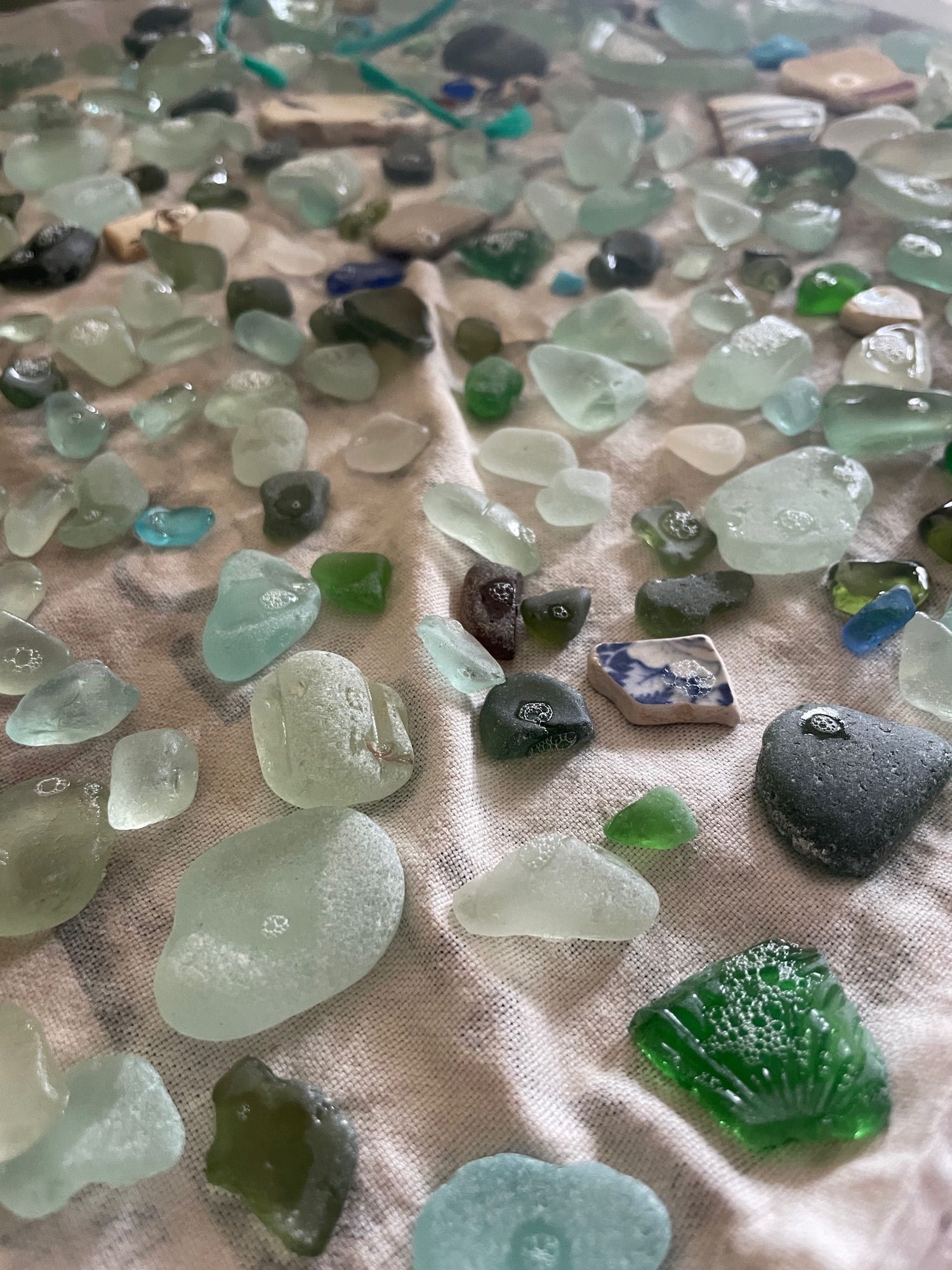 Dozens of pieces if wet sea glass, some with suds in, resting on a tea towel