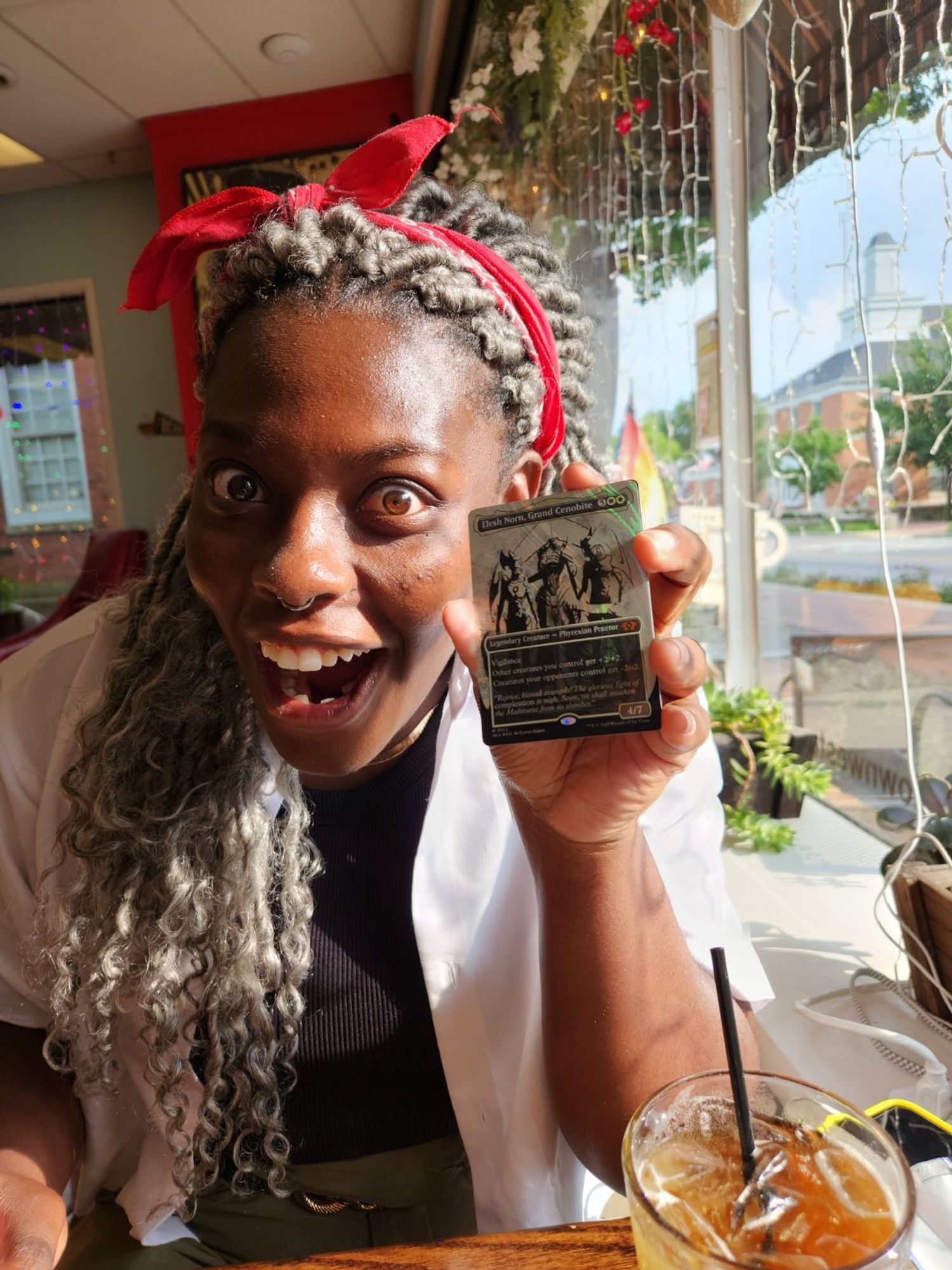 A person, elated, in a warm, sunlit cafe holding the magic card Elesh Noorn while gawk at the card unbelievably. 
