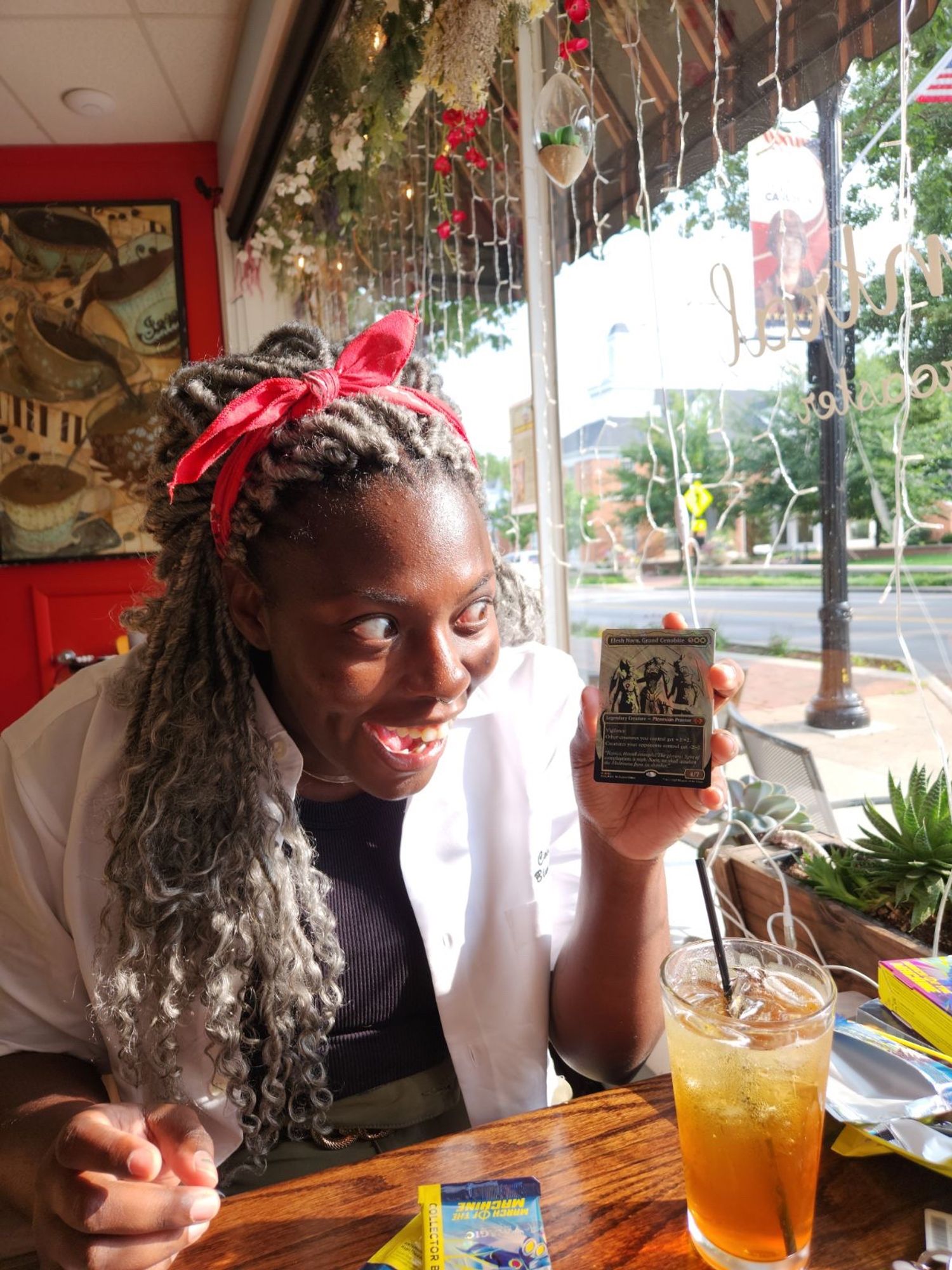 A person, elated, in a warm, sunlit cafe holding the magic card Elesh Noorn while gawking at the card unbelievably. There are packs of Magic the Gathering Aftermath lying around. 
