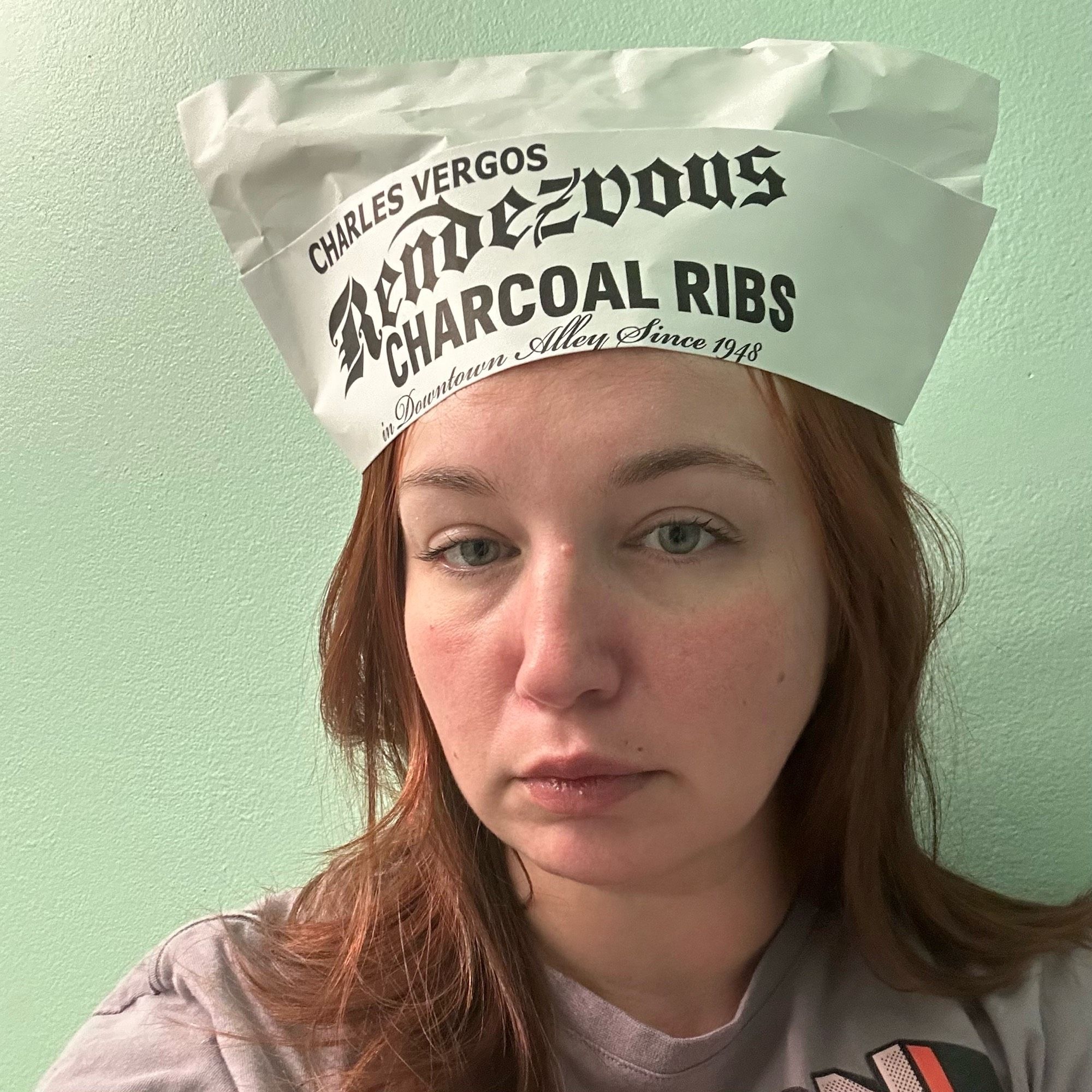 Me in front of a blue wall wearing a paper hat from Rendezvous in Memphis. Not smiling because there is no bbq in front of me yet.