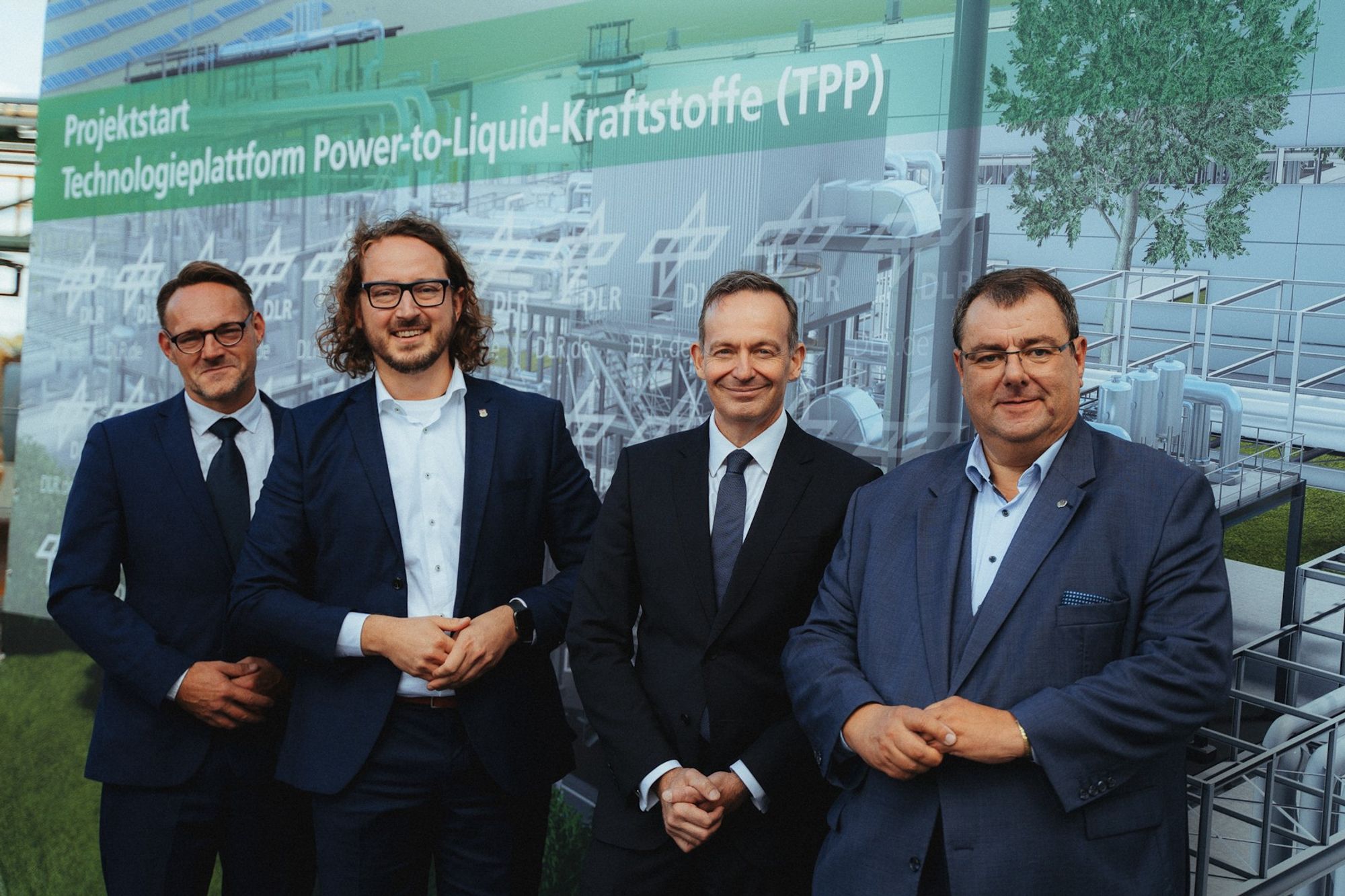 Gruppenfoto mit Volker Wissing in Leuna. Im Hintergrund sieht man ein großes Banner auf dem steht: Projektstart Power-to-Liquid-Kraftstoffe (TPP).