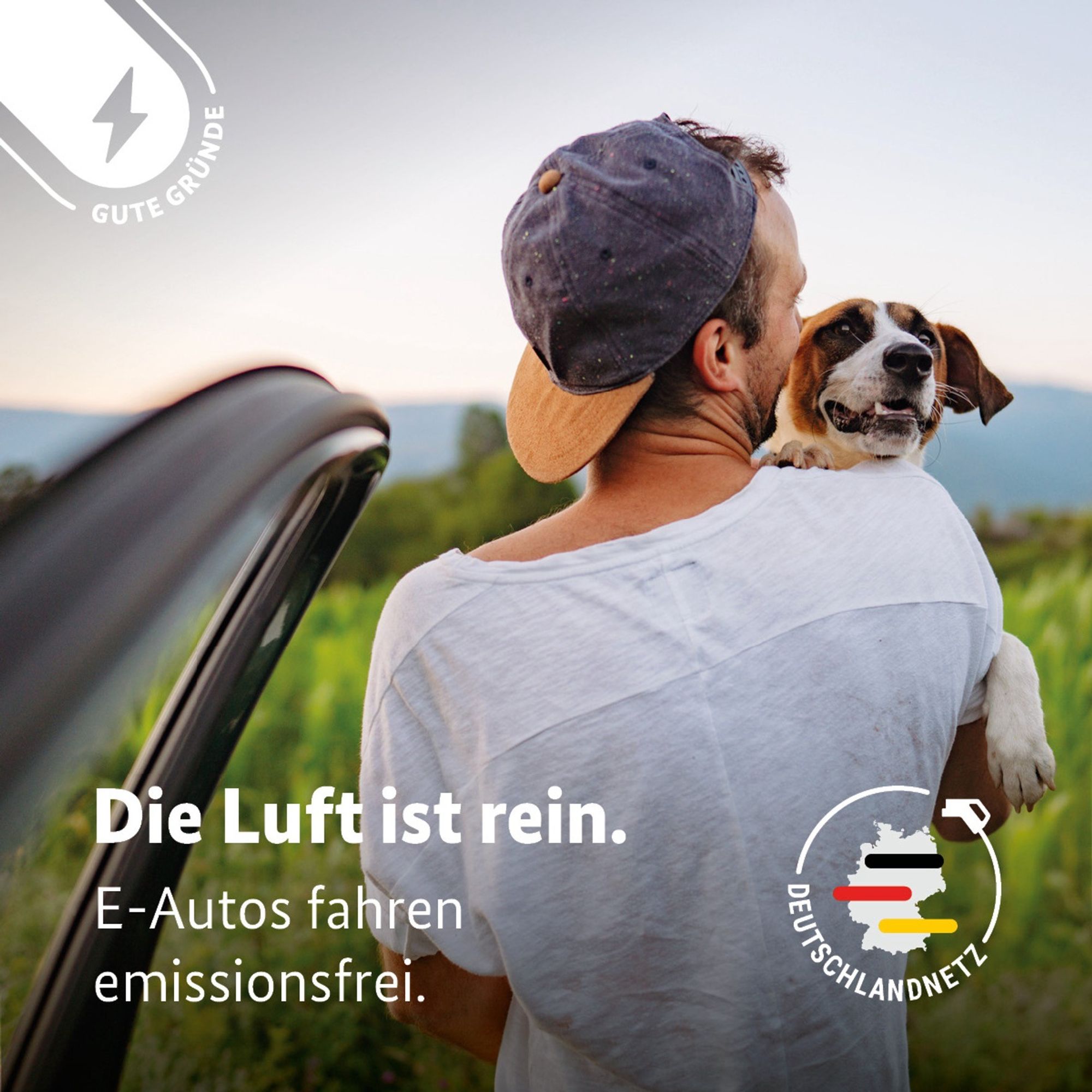 Auf der Grafik ist ein Foto eines Mannes zu sehen, der einen Hund trägt und aus dem Auto ausgestiegen ist, im Hintergrund sind Wiesen und Wälder zu sehen. Als Text steht auf der Grafik: Die Luft ist rein. E-Autos fahren emissionsfrei. Rechts unten ist das Logo vom Deutschlandnetz zu sehen, eine Deutschlandkarte mit einem schwarzen, einem roten und einem goldenen Balken, umrandet von einem Ladeschlauch mit dem Text Deutschlandnetz.