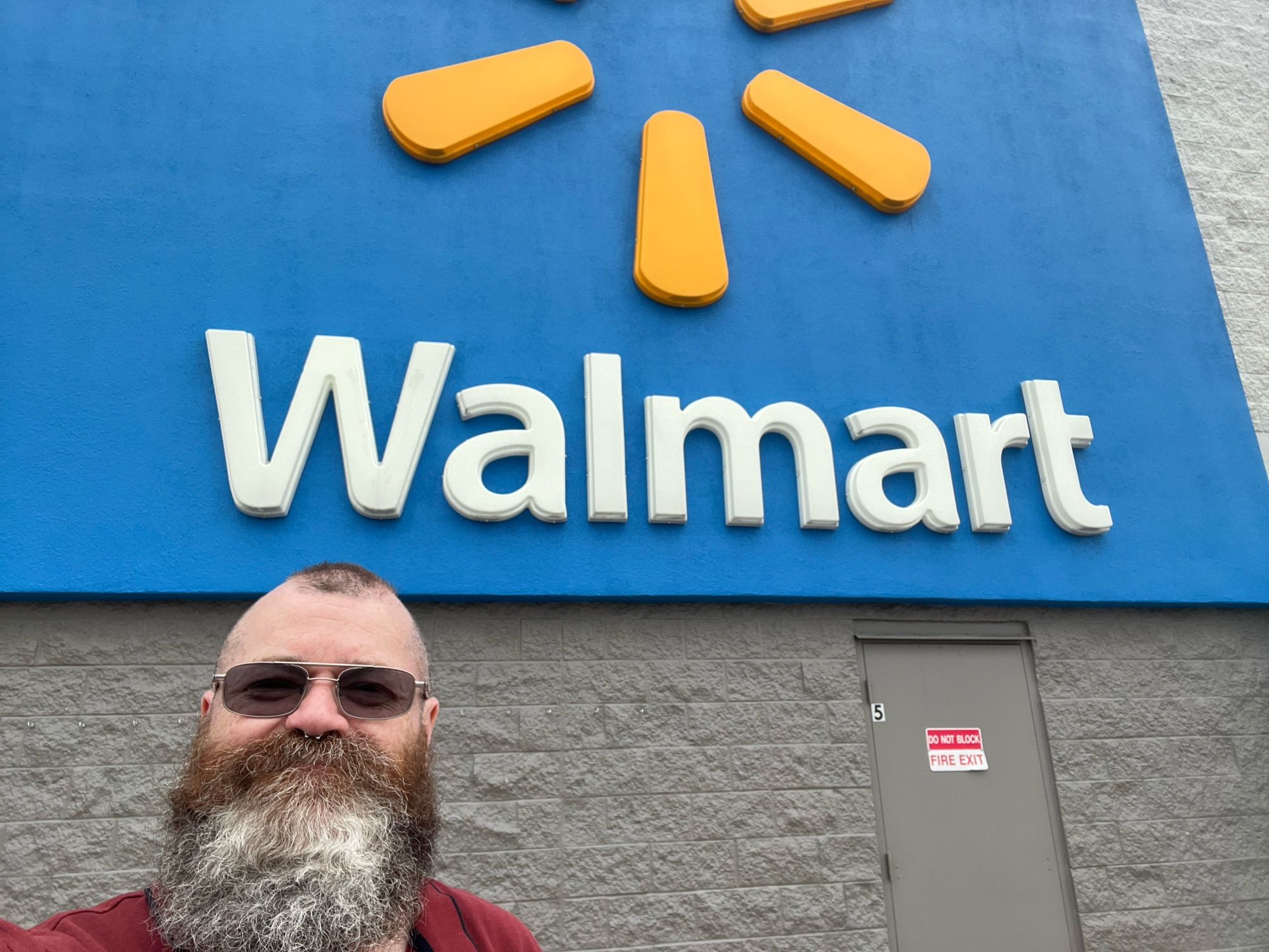 Bearded man wearing sunglasses, standing in front of a Walmart sign