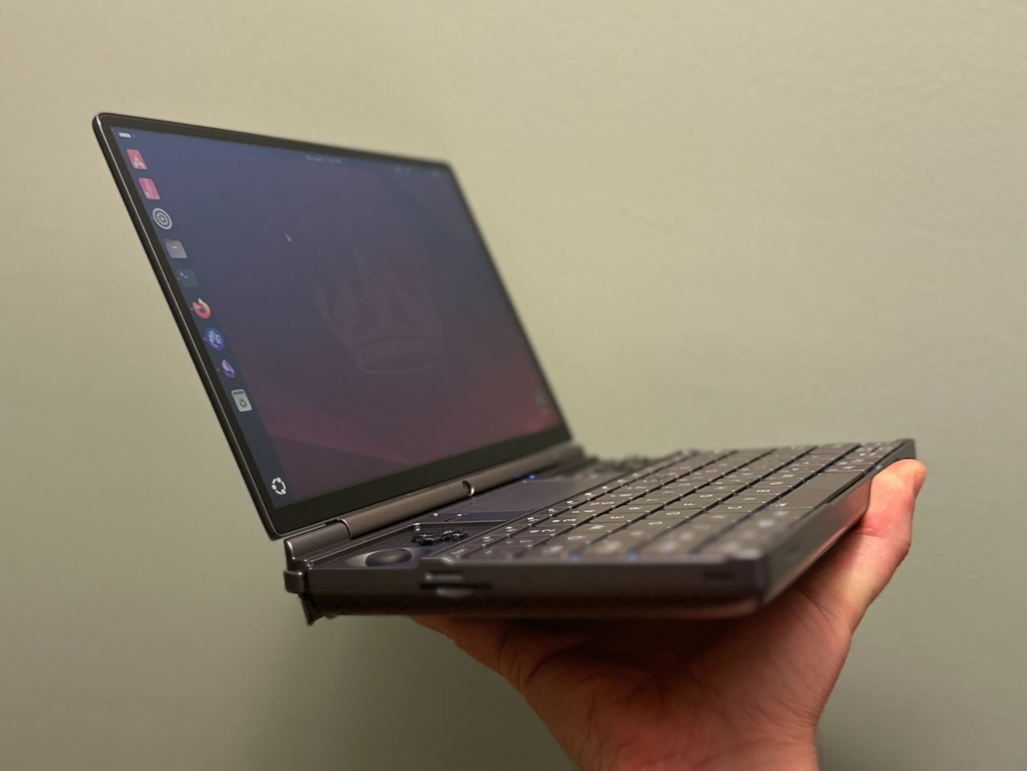 Photo of a GPD 10" mini-laptop in someone's hand, with the Ubuntu 24.04 desktop visible on the screen.