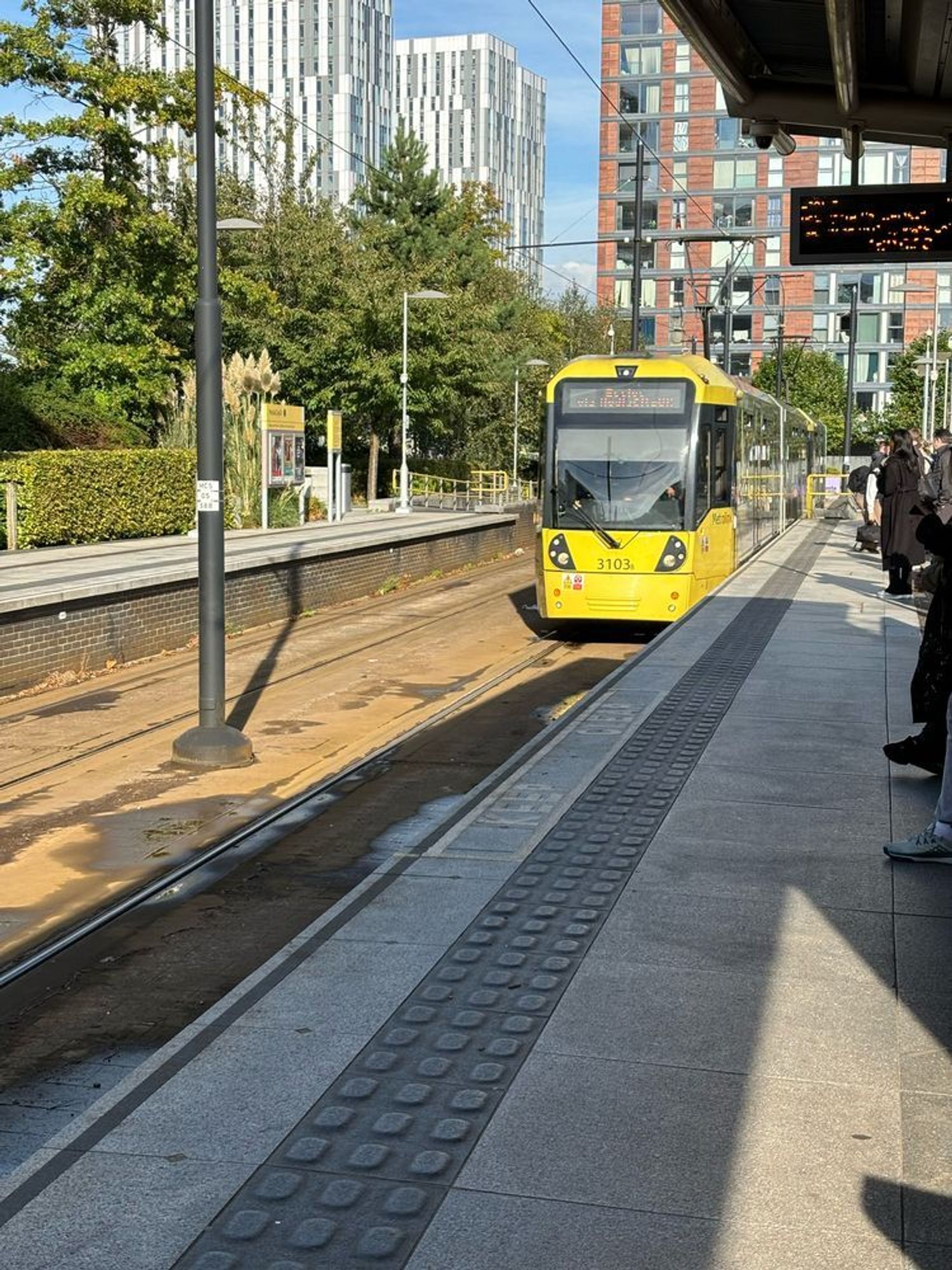 A yellow Manchester Metrolink tram pulling into a stop.