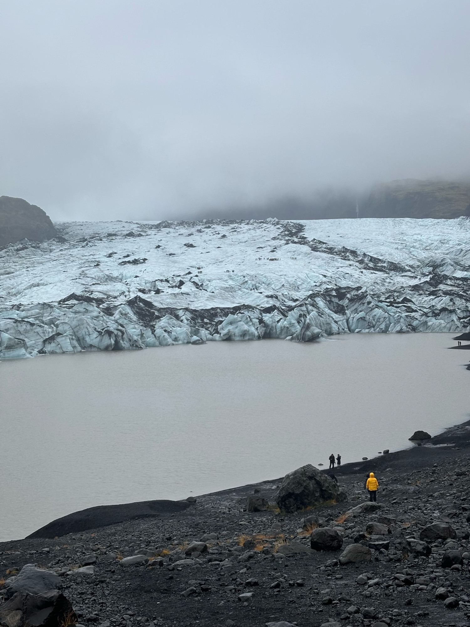 This is the Sólheimajökull glacier sitting behind its glacial lagoon. There are tiny people in the foreground for scale