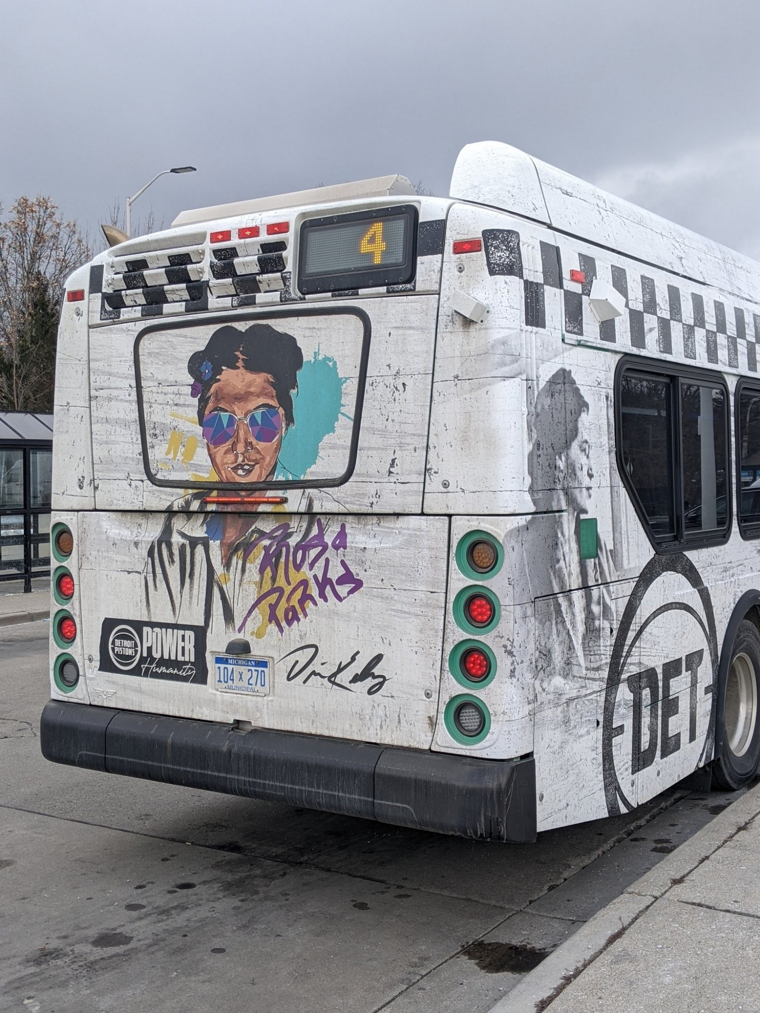 A vibrant rendition of Rosa Parks, wearing tinted shades, on the back of a DDOT bus in Detroit