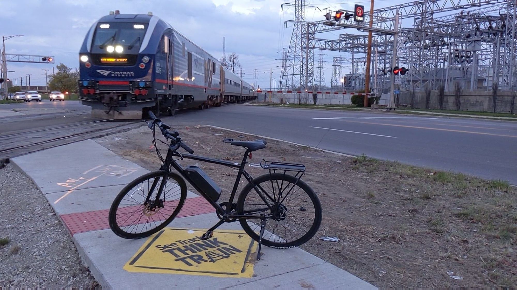 My bike on top of a "See Tracks Think Train" sidewalk stencil next to a railroad crossing in Pontiac as the Wolverine passes by