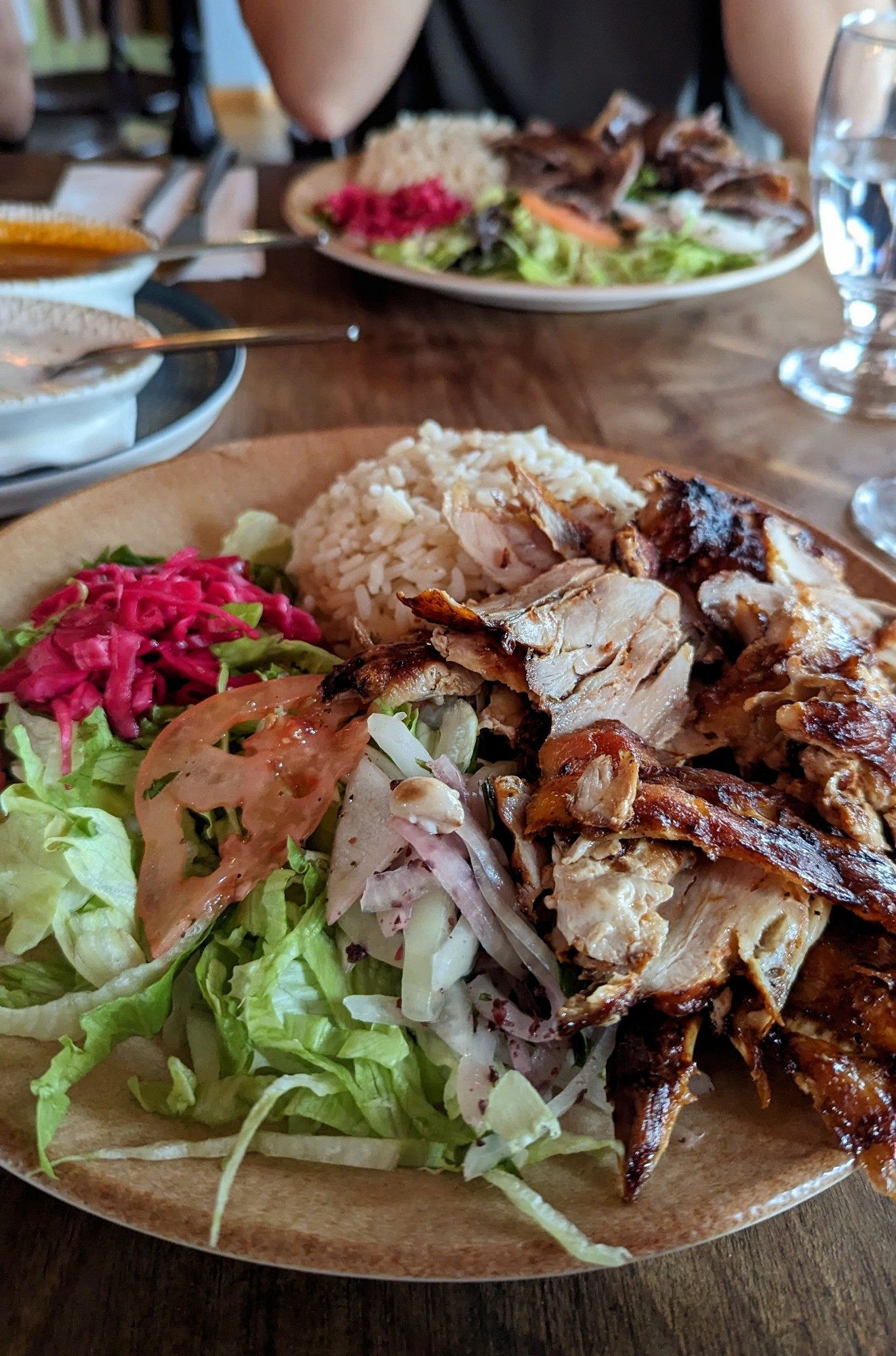 Turkish chicken doner platter with rice, a bed of lettuce, tomato, and pickled vegetables 