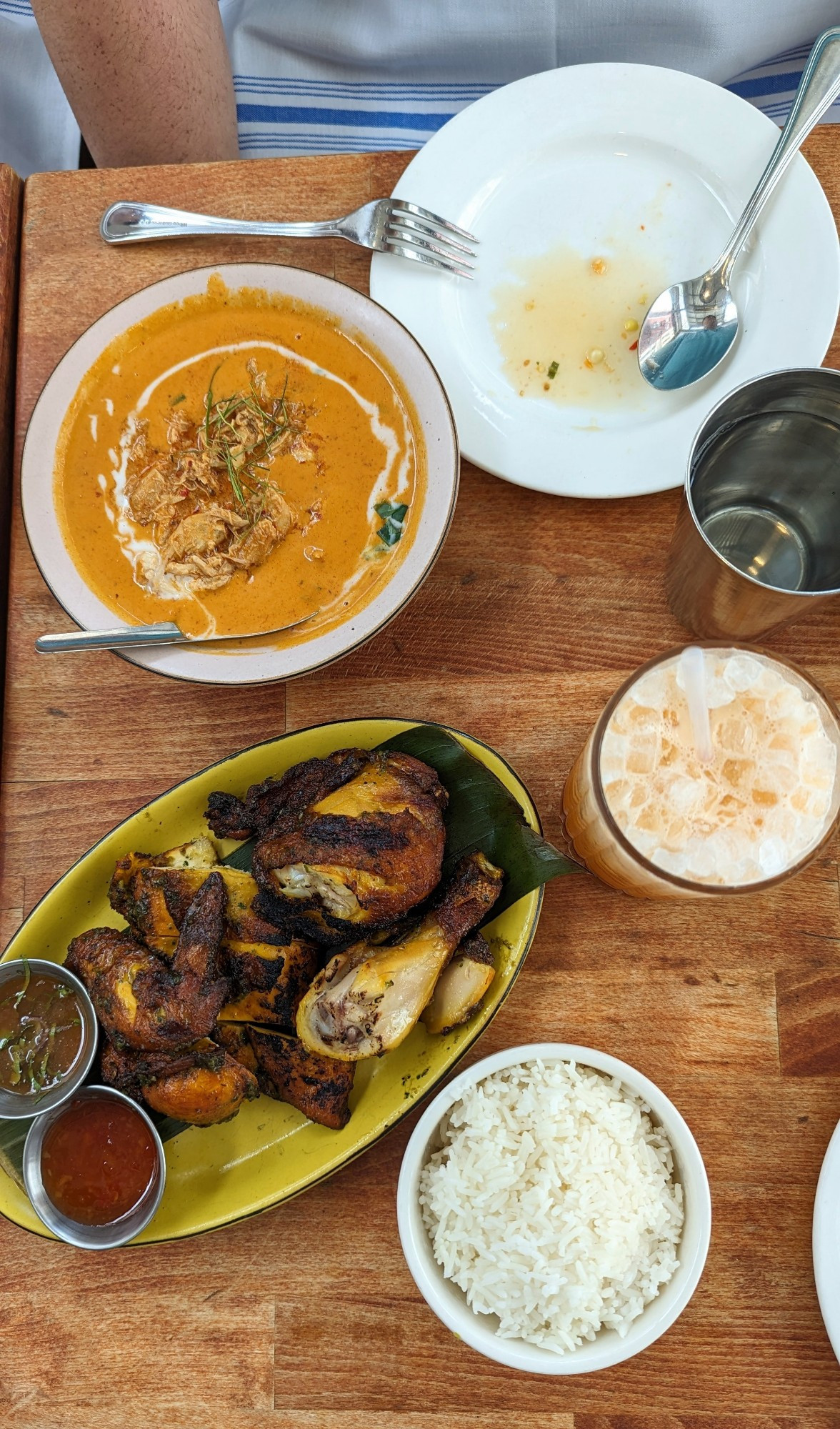 Top down image of a Thai roasted chicken, a bowl of rice, a spicy chicken curry, and a tall glass of Thai iced tea
