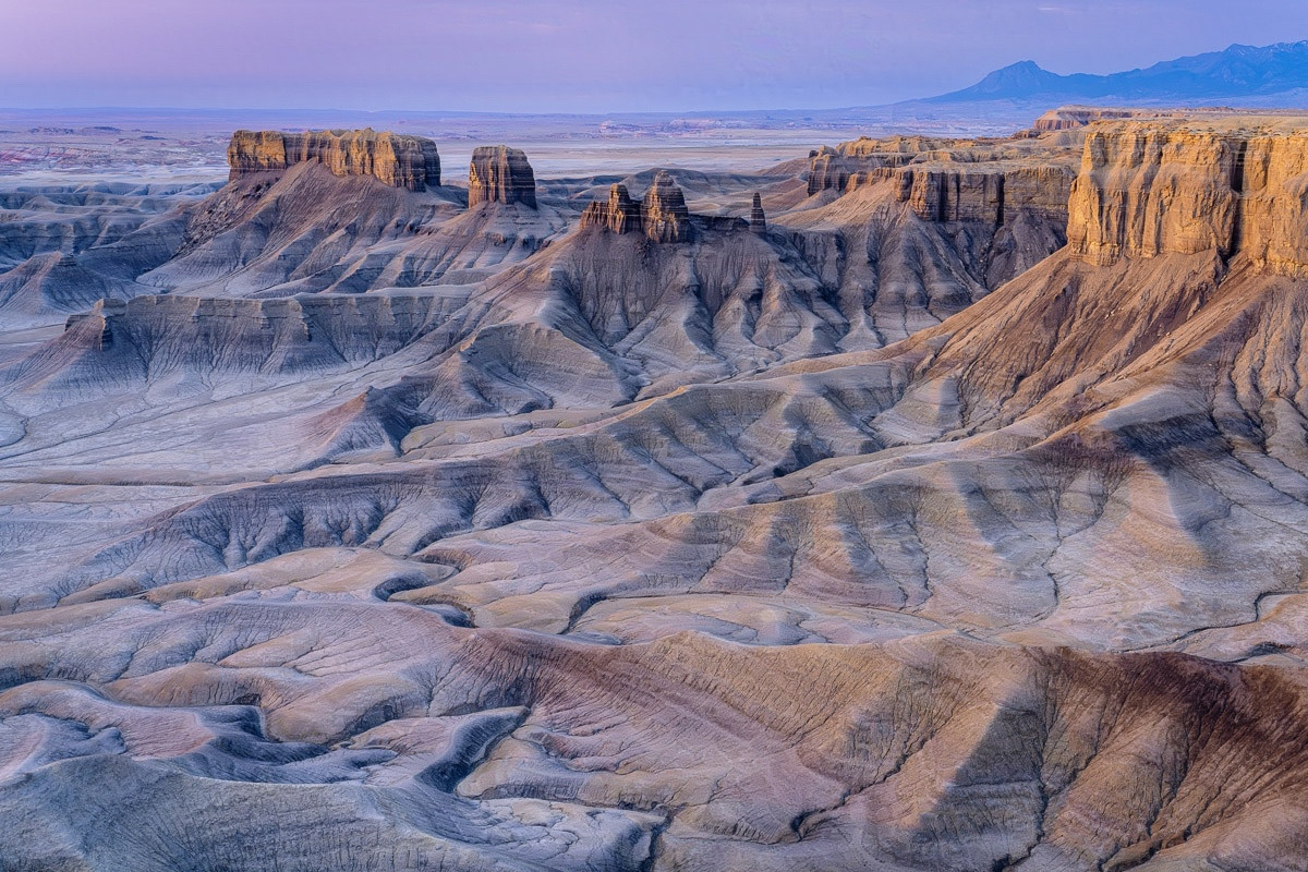 Badlands at sunrise.

The sun is rising to the left in this scene, illuminating a badlands wall and butte. Toward the bottom the rock wall flows into ridges and valleys, forming unusual shapes. Toward the top the sky has a purple/pink hue, tending toward blue on the right.

The sun provides a rich, warm golden color to the rocks in the center.