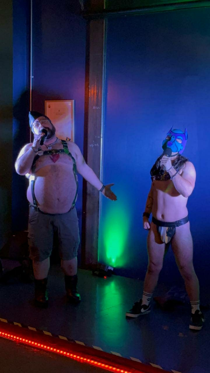 Leather boy and human pup singing on stage. Human pup is now wearing a leather thong with the bear flag design on the pouch