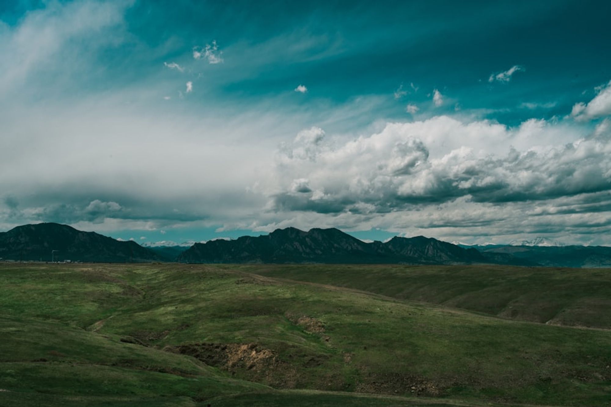 An empty prairie under a gloomy cloudy sky, with a row of low, dark hills in the distance