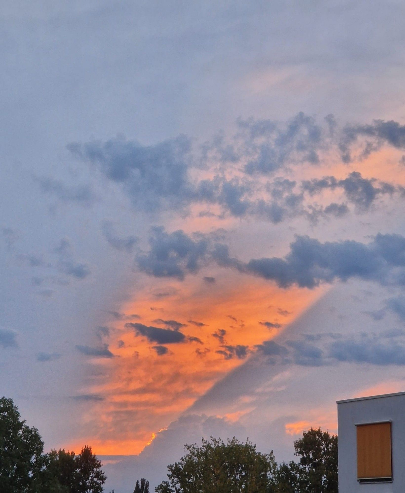 durch die Wolkendecke bricht ein oranger Sonnenstrahl der untergehenden Sonne, fast wie mit dem Lineal gezogen