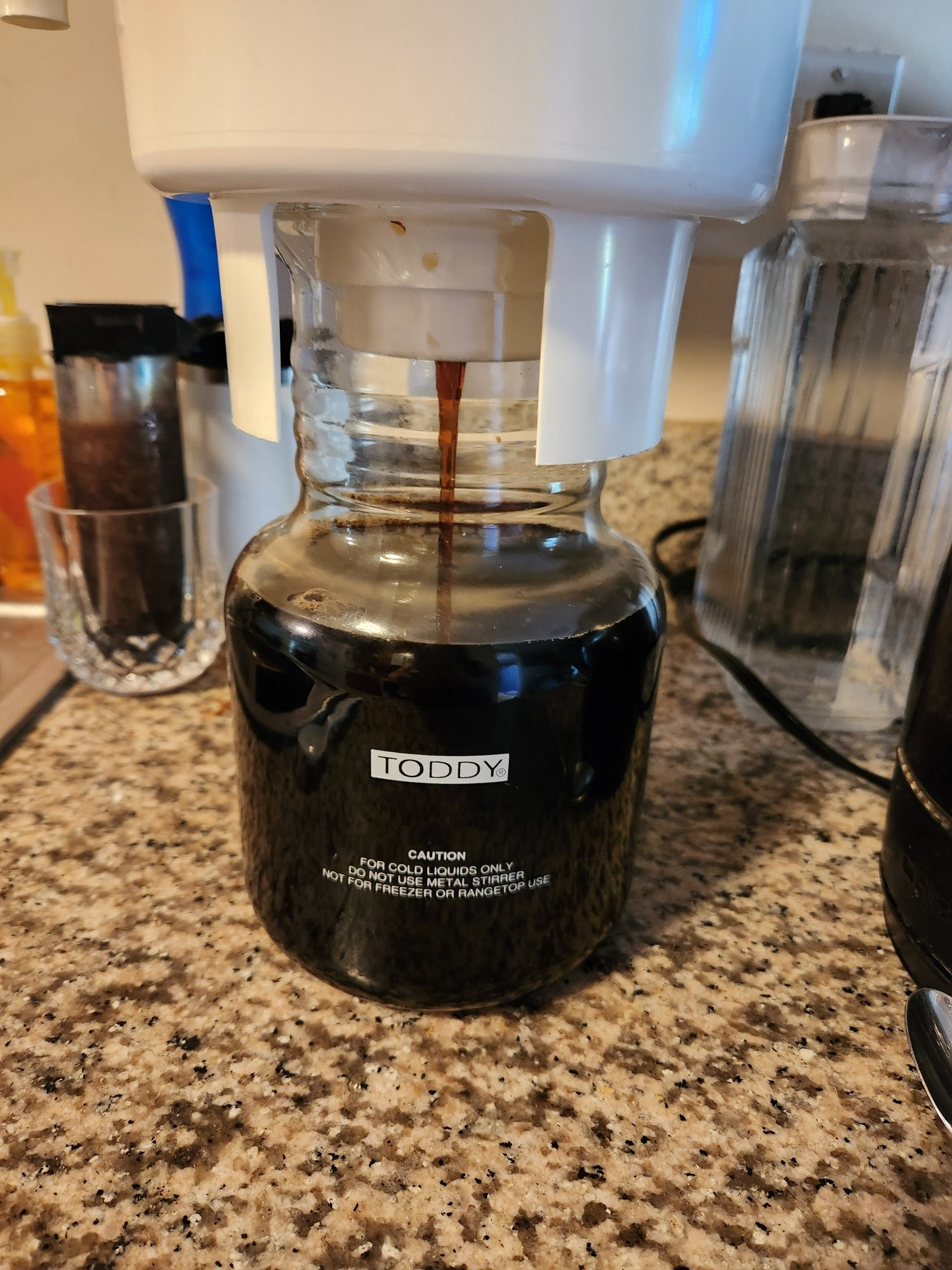 Coffee concentrate exiting the brewing container by gravity extraction, filling a Toddy brand glass carafe.