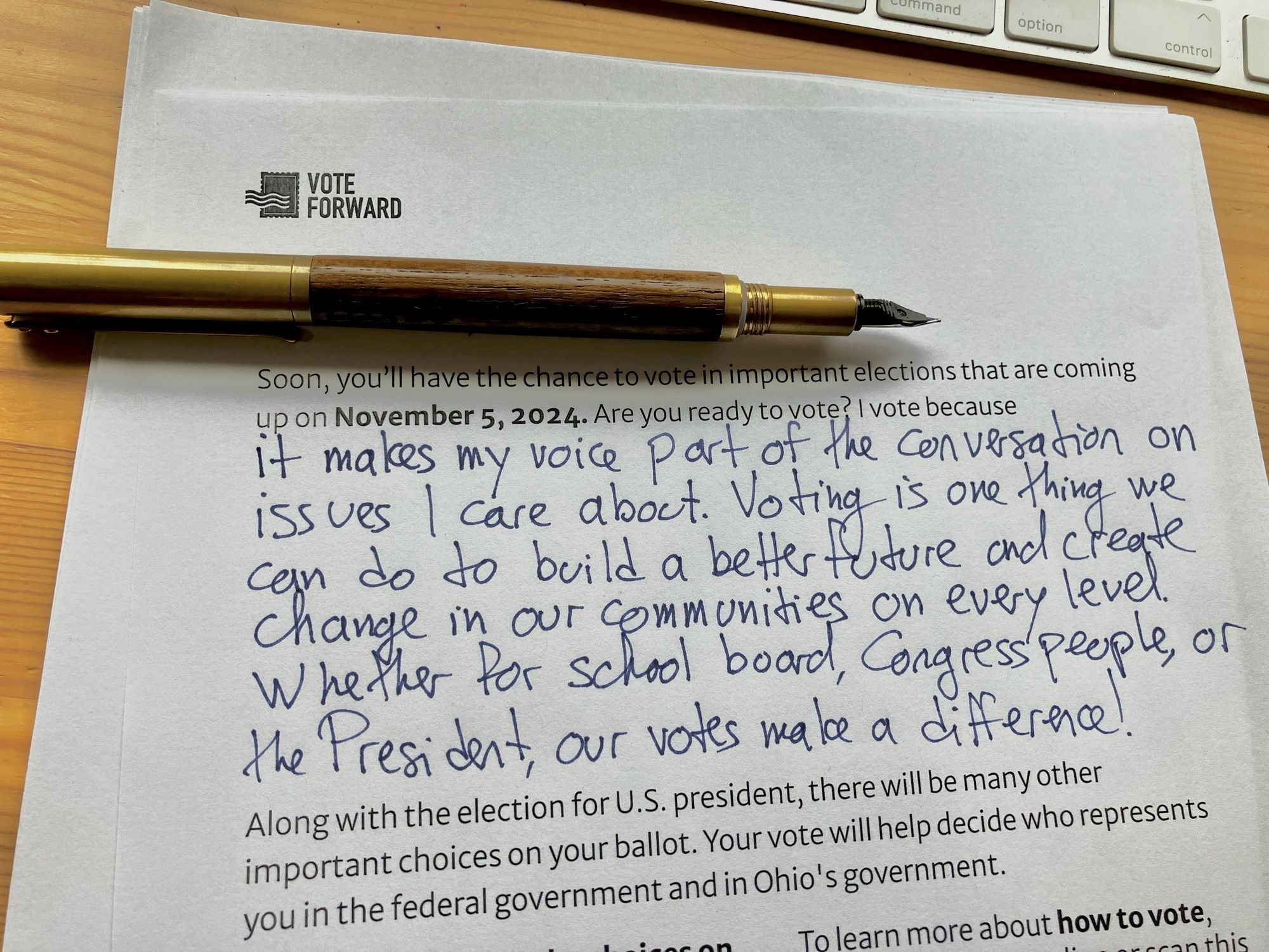 A brass and teak fountain pen rests atop a partially typed partially handwritten letter encouraging someone to vote. The header is by Vote Forward.