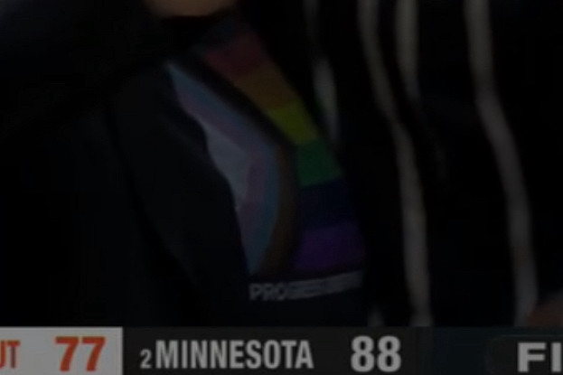 Closeup of Cheryl reeve’s shirt from an ESPN screencap. It shows the LGBTQIA+ flag with a caption underneath; the one legible word is “progress”