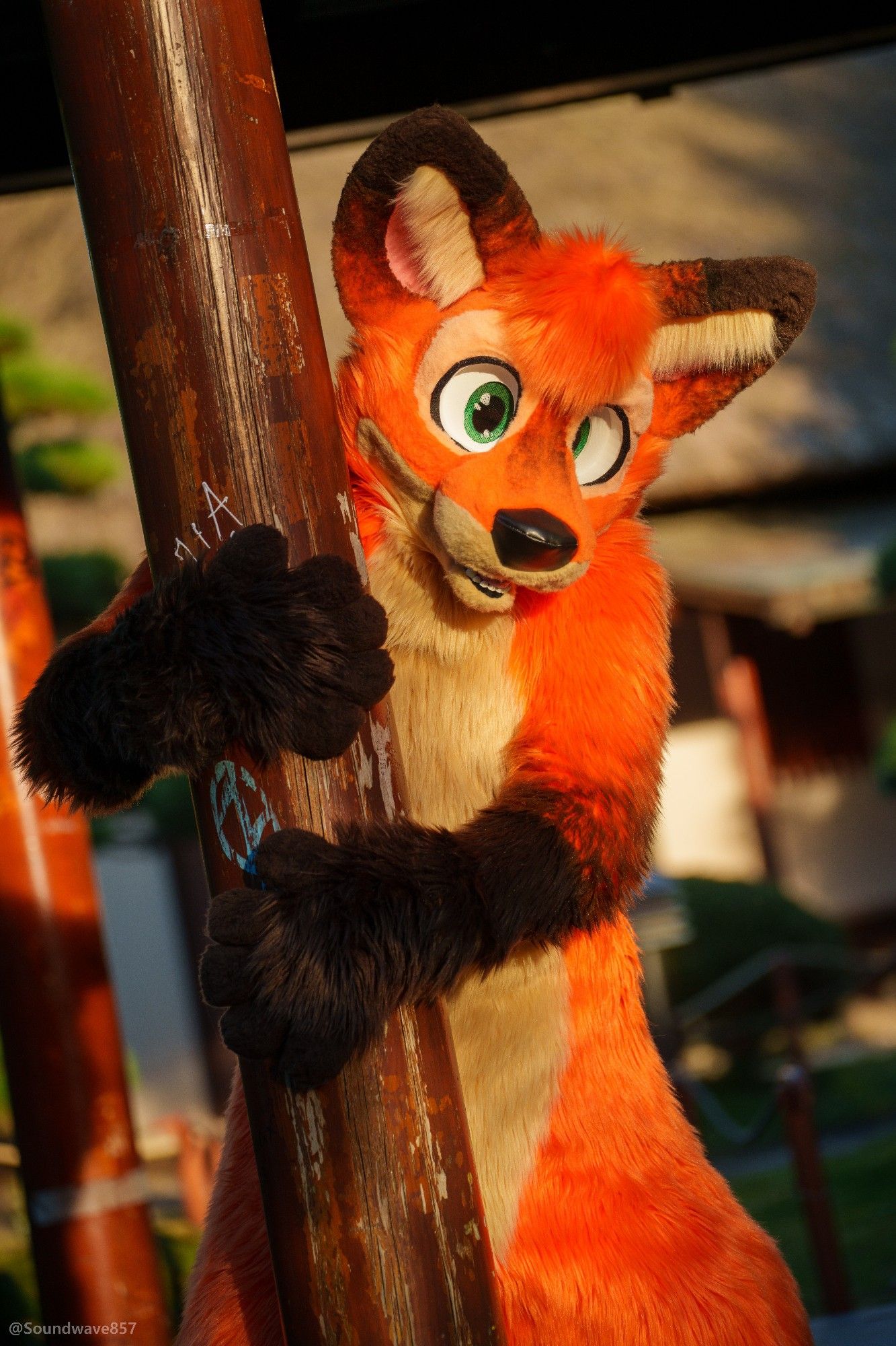 Vozzy, red fox fursuiter embracing a pole at a Japanese garden in Hamburg