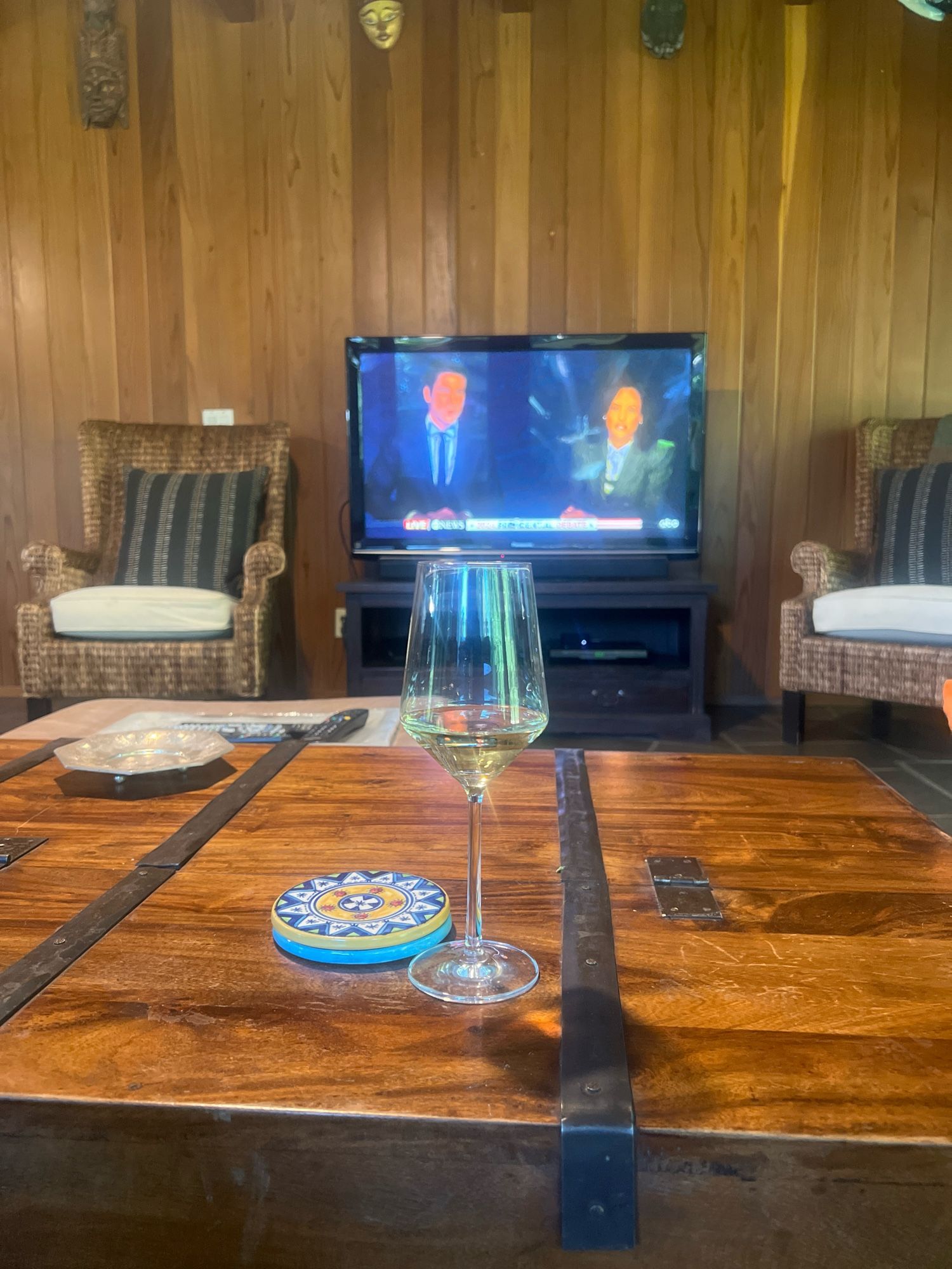 A glass of wine on a trunk table in front of a TV showing the hosts for the presidential debate.