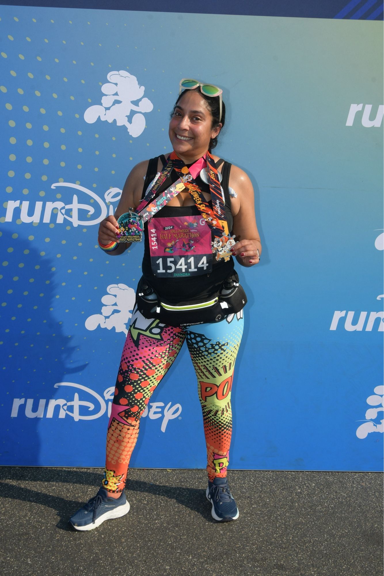 Diandra in colorful leggings holding aloft two medals post half marathon.