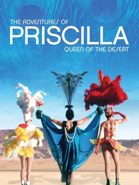 Poster image for the Adventures of Priscilla Queen of the Desert, three gals in extravagant show outfits, in front of a desert landscape.