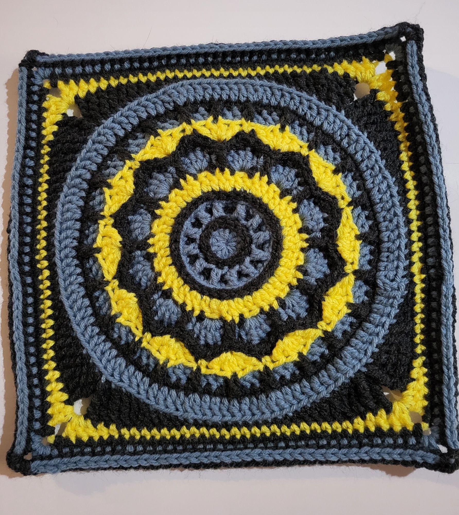 Crochet block, mandala pattern in blue, dark grey, and yellow