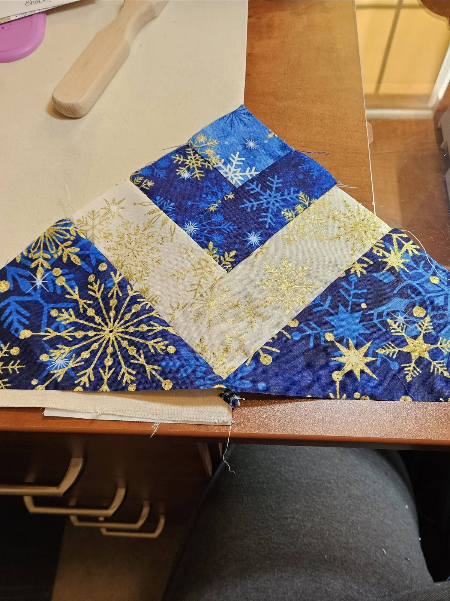 Lattice pieced triangle alternating light gold and white snowflake fabric with gold snowflake on dark blue fabric and a small square of gold snowflake on lighter blue fabric top.