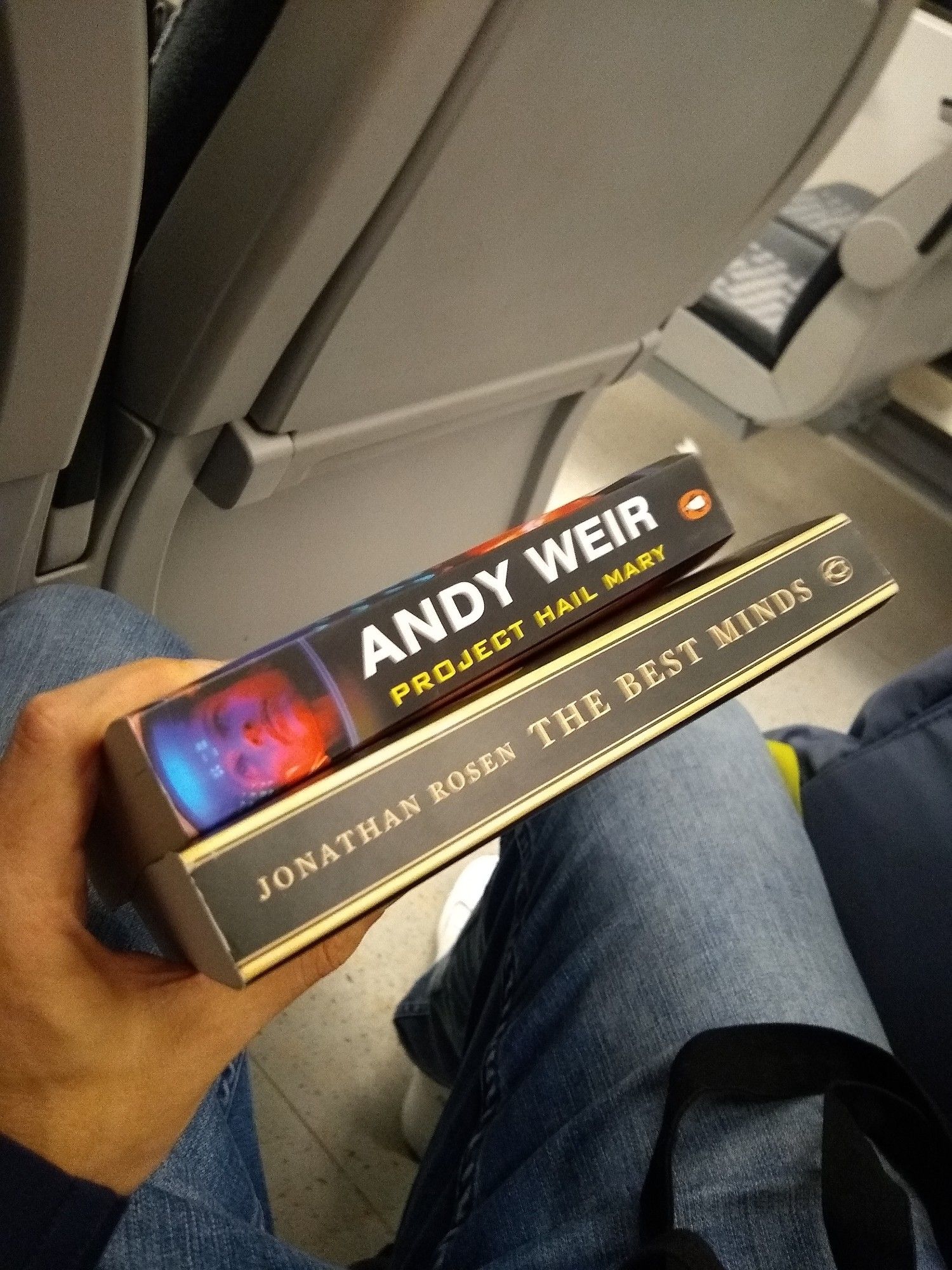 Ein Foto davon, wie ich zwei Bücher in meiner Hand in einem Zug halte. Das eine ist "Project Hail Mary" von Andy Weir, das andere "The Best Minds" von Jonathan Rosen.