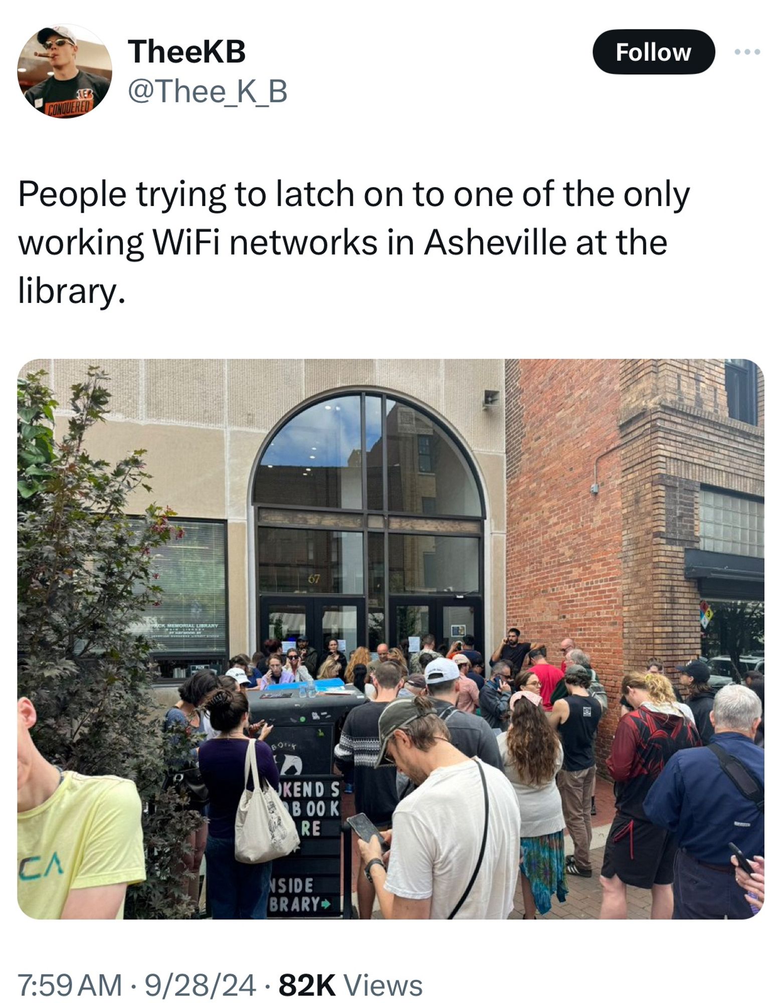 Crowd of people looking at devices outside the glass doors;

People trying to latch on to one of the only working WiFi networks in Asheville at the library.