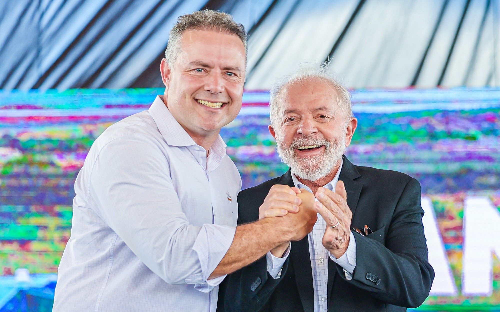 Na foto, o presidente Lula sorri ao lado do ministro dos Transportes Renan Filho. Os dois estão de mãos dadas e sorrindo para a foto.