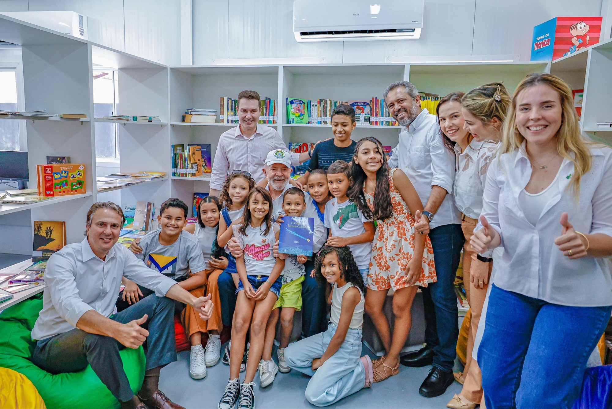 Na foto, o presidente Lula sorri ao lado de crianças moradoras do conjunto habitacional Cidade Jardim I Módulo IV, no Conjunto José Walter, em Fortaleza (CE). Ao lado deles, a comitiva do governo federal e do estado. Eles estão dentro da biblioteca do empreendimento do Minha Casa, Minha Vida.