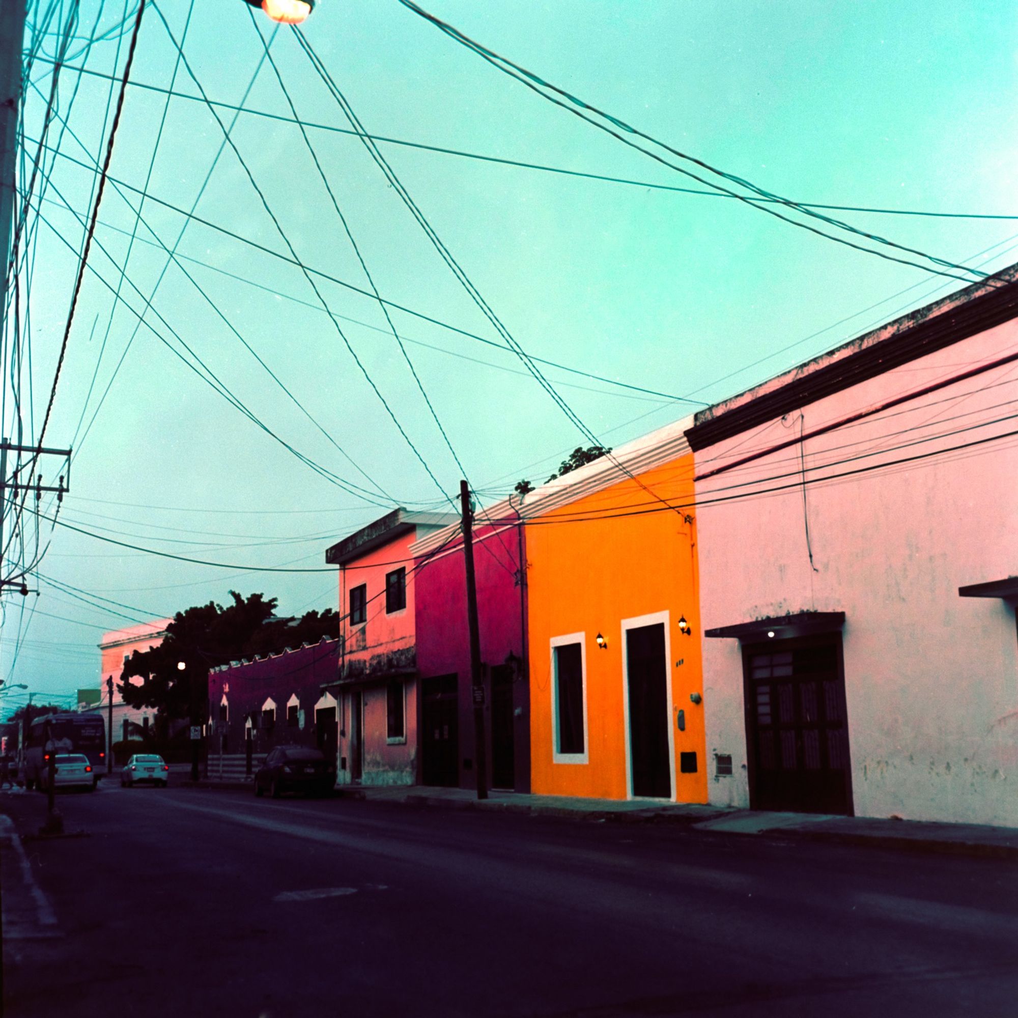 A street at dusk in Merida, Mexico. The buildings are colorful. Telephone wires tie it all together.