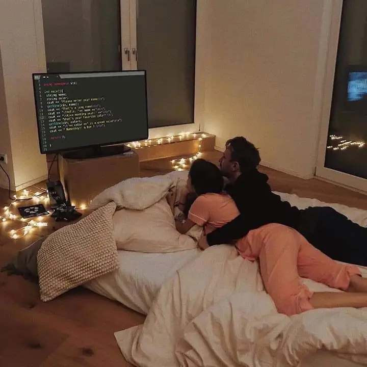 couple lying on the bed in romantic atmosphere looking at a big screen with code in front of them