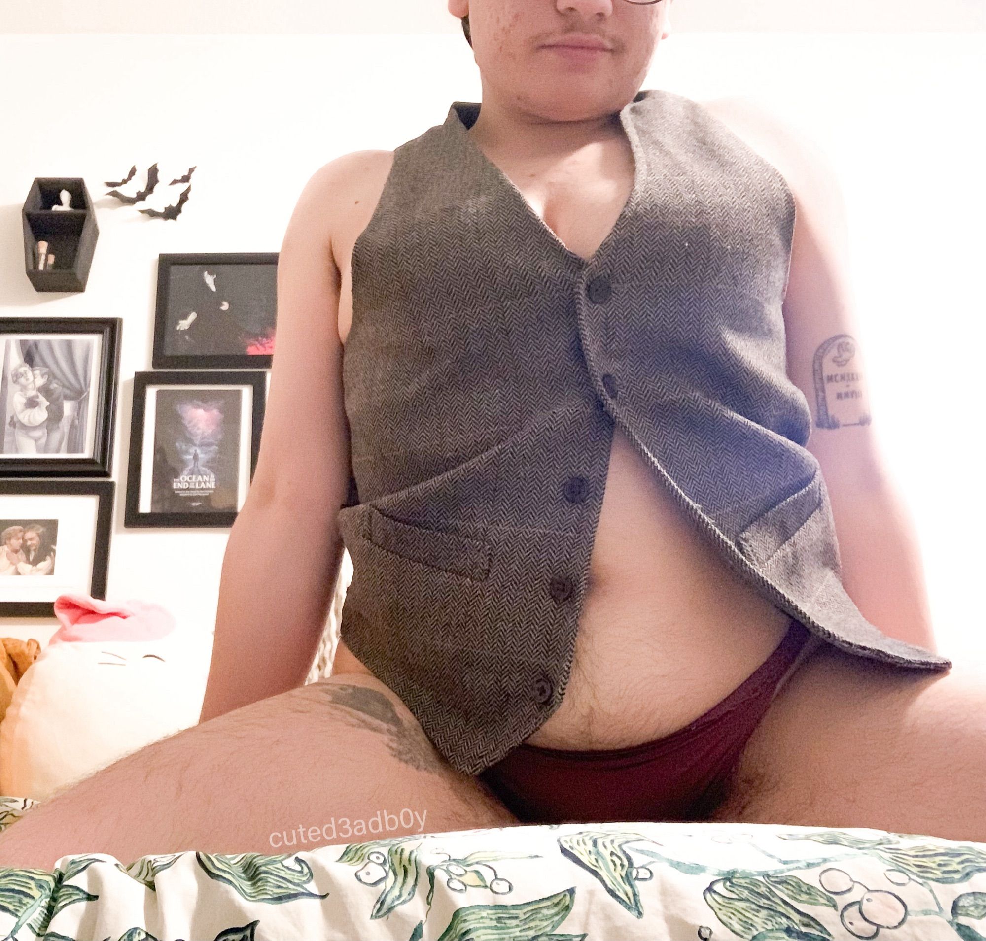 Prince sits on his knees wearing a tweed vest with nothing underneath and dark pink lacey panties. He’s smirking at the camera