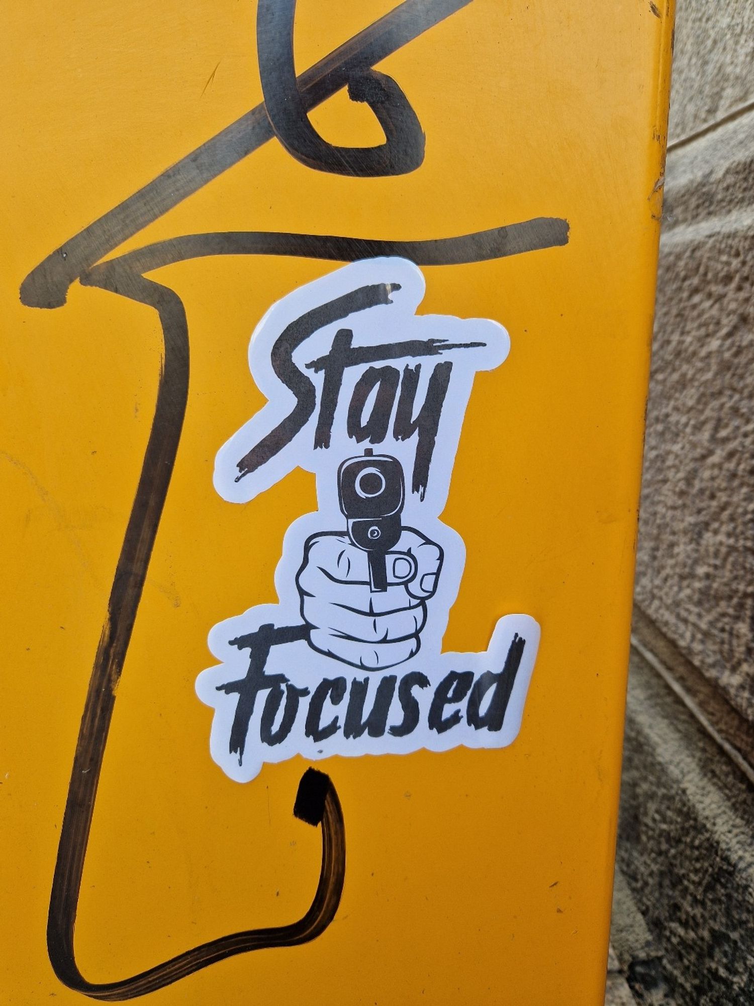 A big sticker on the side of an orange postbox. The sticker has a hand pointing a gun straight ahead and text "stay focused"