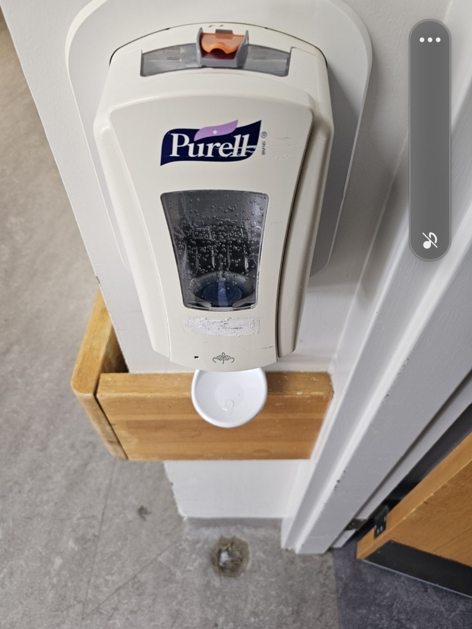 Purell dispenser with a hole below it where the floor has been partially eaten away by hand sanitizer drips.