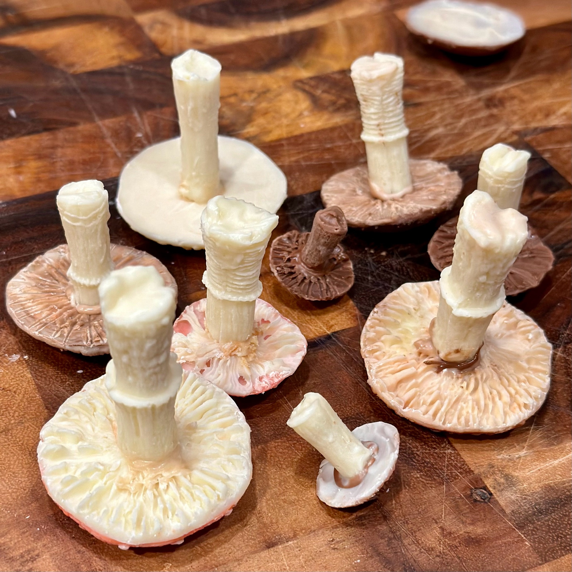 Several chocolate mushrooms set on a wooden cutting board, cap-side-down, gills and stems up