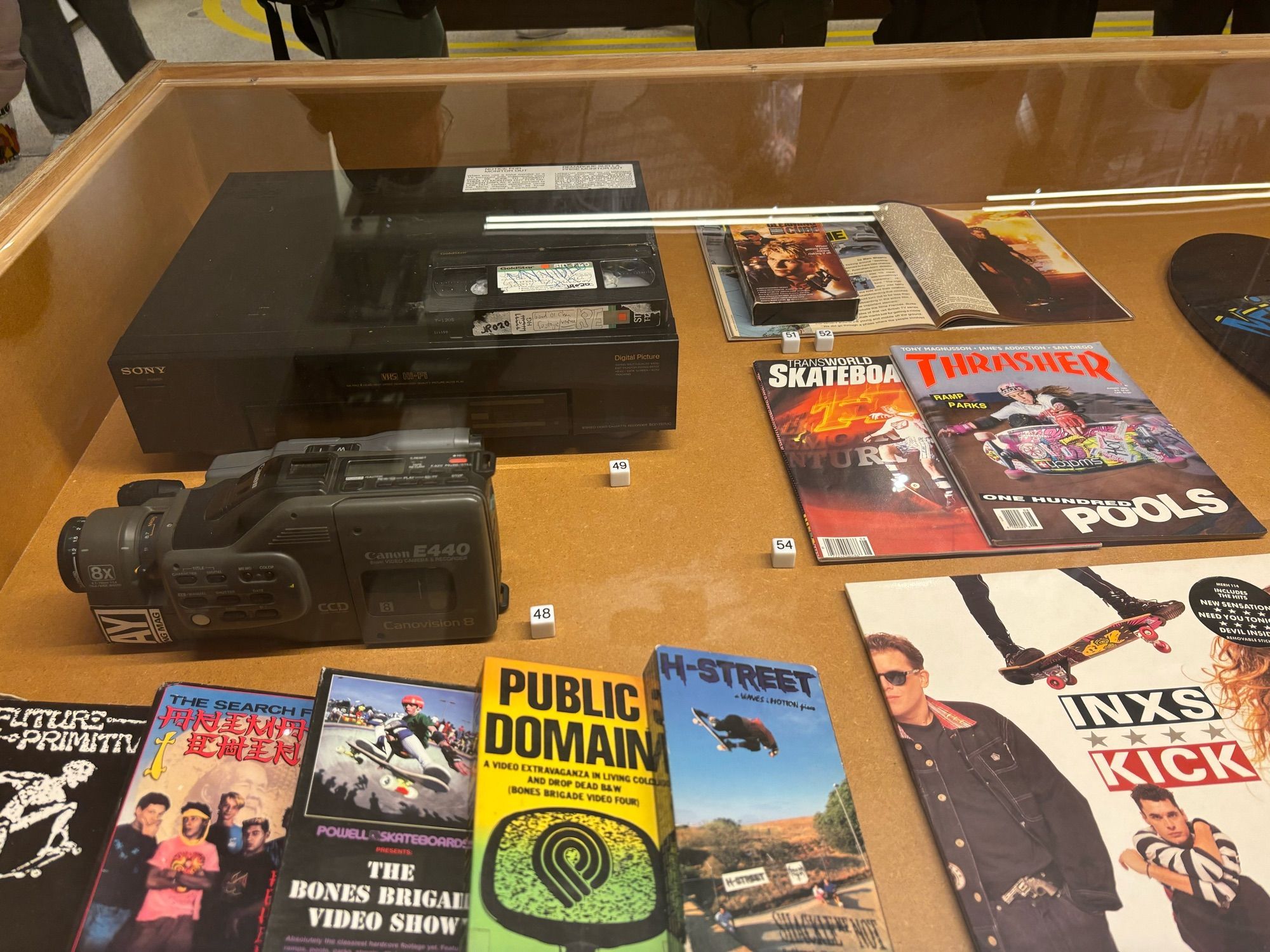 A collection of video tapes, a VCR, a camcorder, magazines and vinyl from skate culture in the 1980s