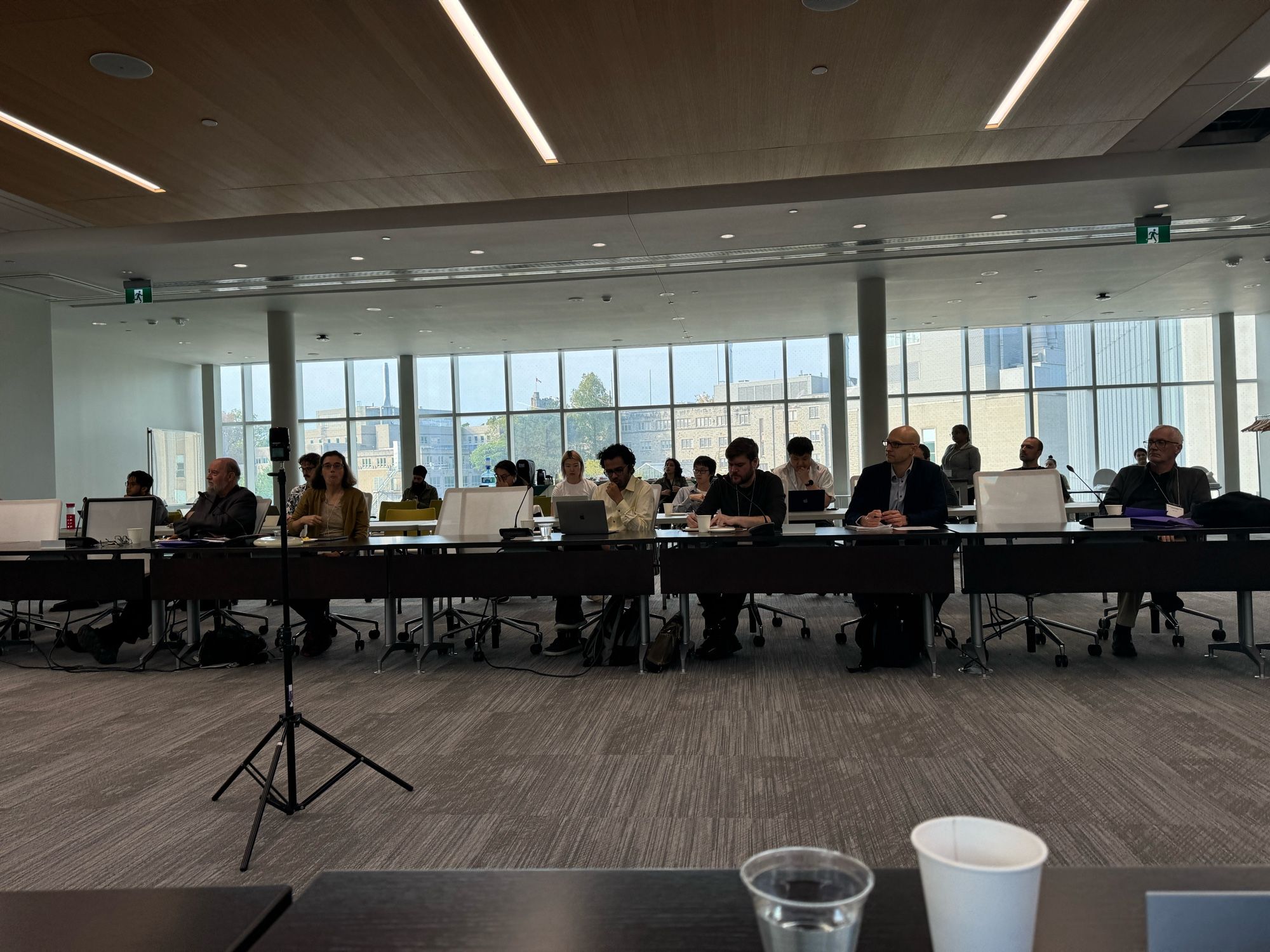 Half of room audience at conference with glass wall in background.