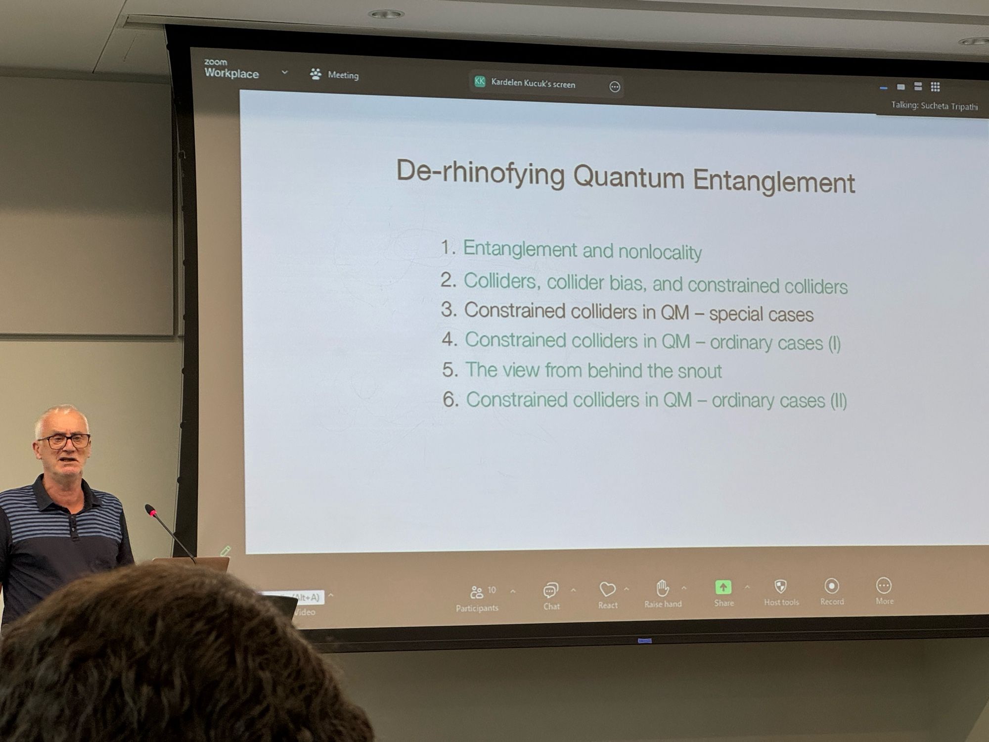 Huw standing in front of screen with text "De-rhinofying Quantum Entanglement
1. Entanglement and nonlocality
2. Colliders, collider bias, and constrained colliders
3. Constrained colliders in QM - special cases
4. Constrained colliders in QM - ordinary cases (I)
5. The view from behind the snout
6. Constrained colliders in QM - ordinary cases (Il)