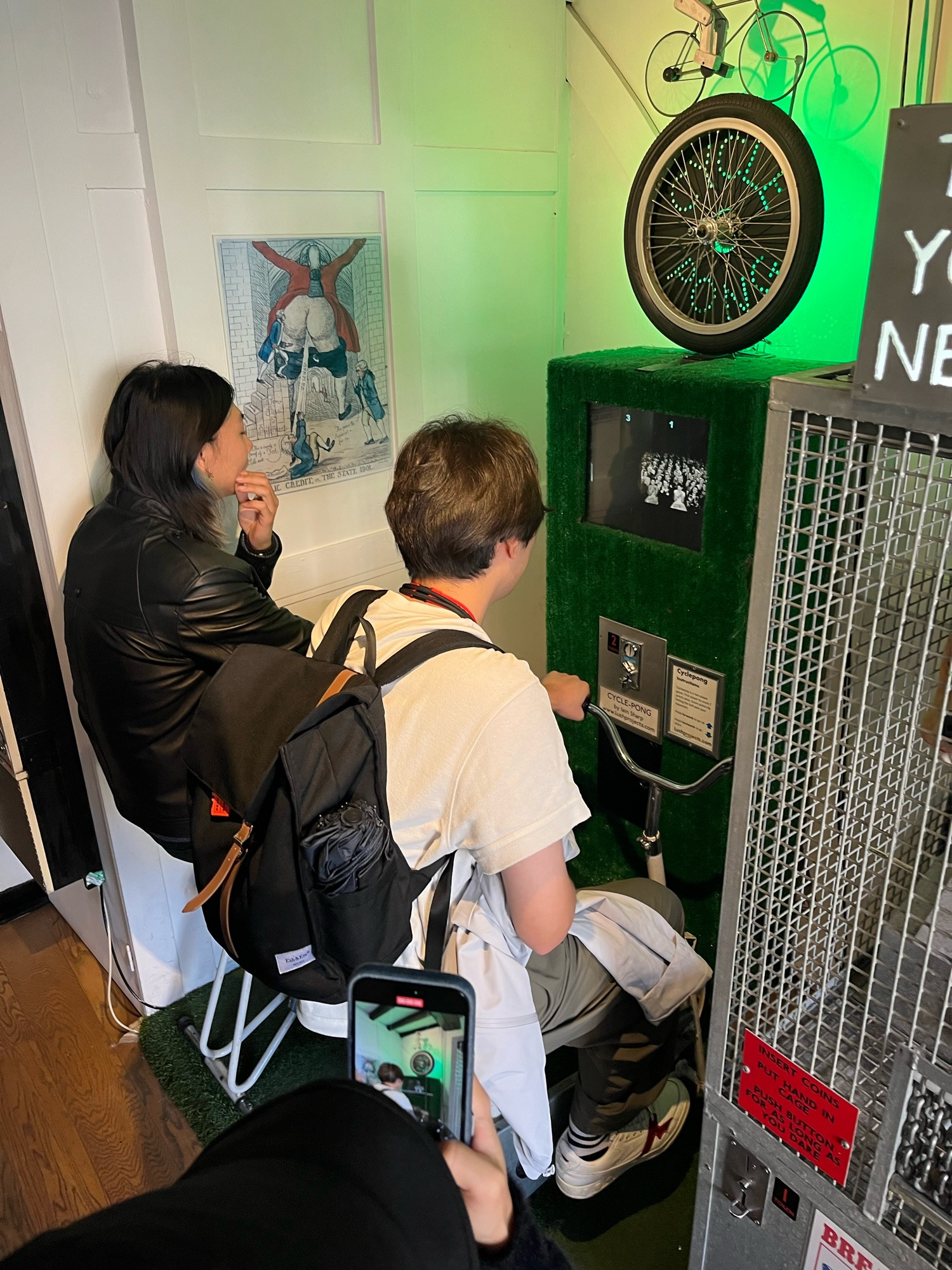 A photo of people playing an arcade game called cycle pong, they both sit on bicycle seats and have to pedal to control the game